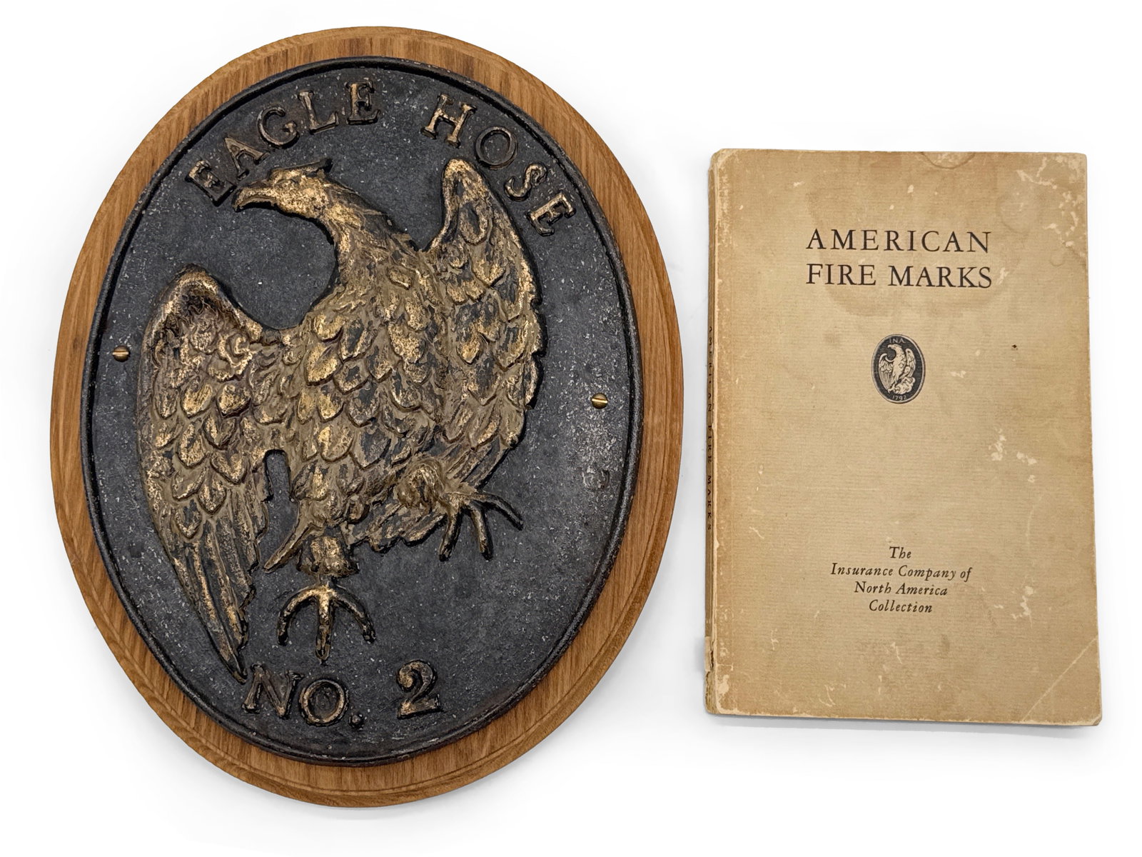 Eagle Hose Cast Fire Mark and Book: A cast iron "Eagle Hose No. 2" fire mark attached to a wooden plaque, and a book of American Fire Marks by The Insurance Company of North America Collection. Fire mark: 11in tall x 8in wide. | You hav
