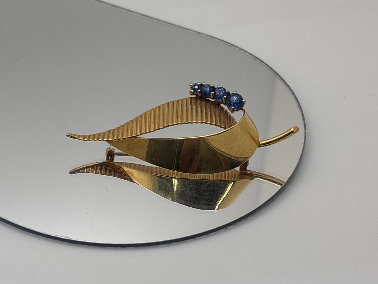 14K Stylized Leaf Brooch with Sapphires: A 14K yellow gold smooth and fluted leaf-form brooch with four graduated sapphires of 4.4mm, 3.6mm, 3.7mm and 2.5mm. Marked 14K. 5.27 dwt. | You have additional shipping options, and are not required