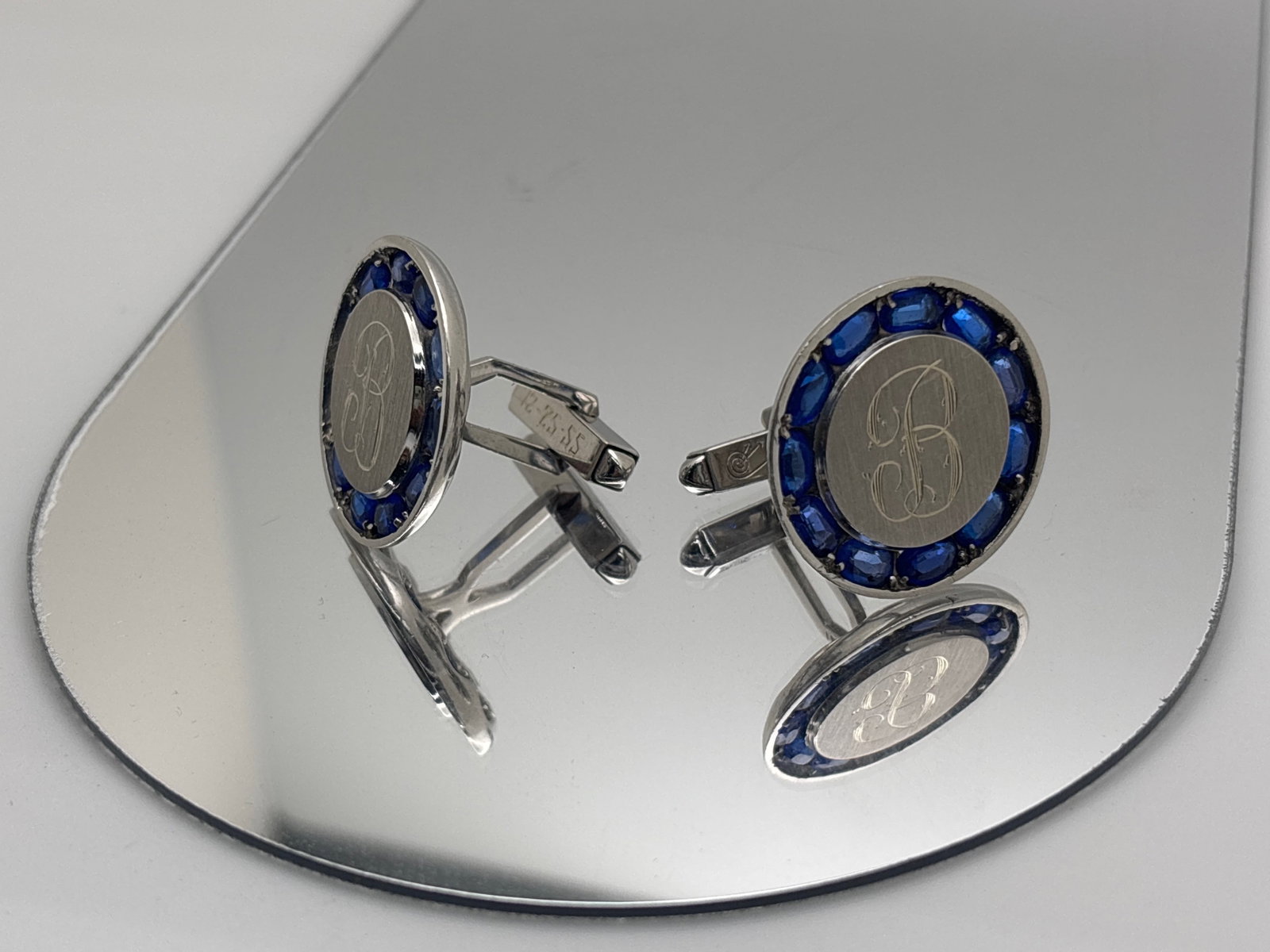 Lucien Piccard 14K and Sapphire Cufflinks: A pair of Lucien Piccard cufflinks in 14K white gold with monogrammed "B" centers and with 11 oval cut sapphires of approx. 4.3mm x 2.5mm, approx. 4.4cts surrounding. Signed Lucien Piccard and marked