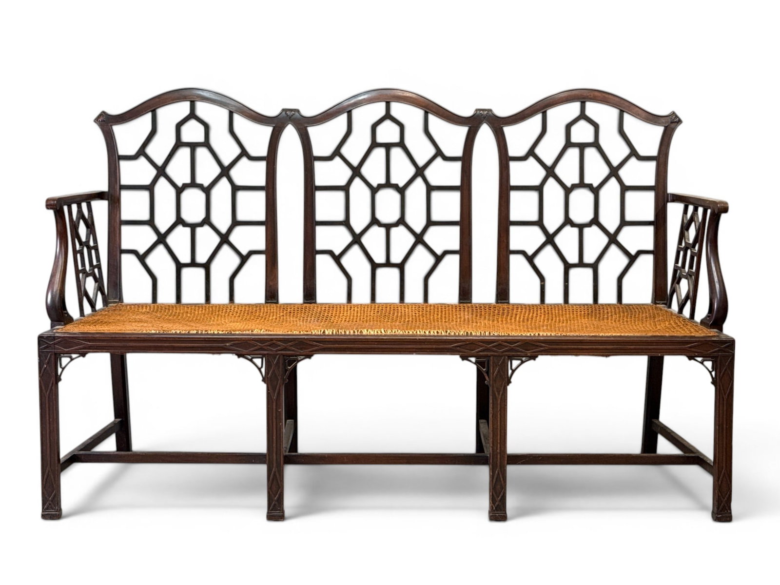 Chinese Chippendale Mahogany Settee: A late 19th/early 20th C. English Chinese Chippendale carved mahogany triple chair-back settee with piecework backs, caned seat, and stretcher frame. Made in England tag. 40in tall x 62in wide x 20in 