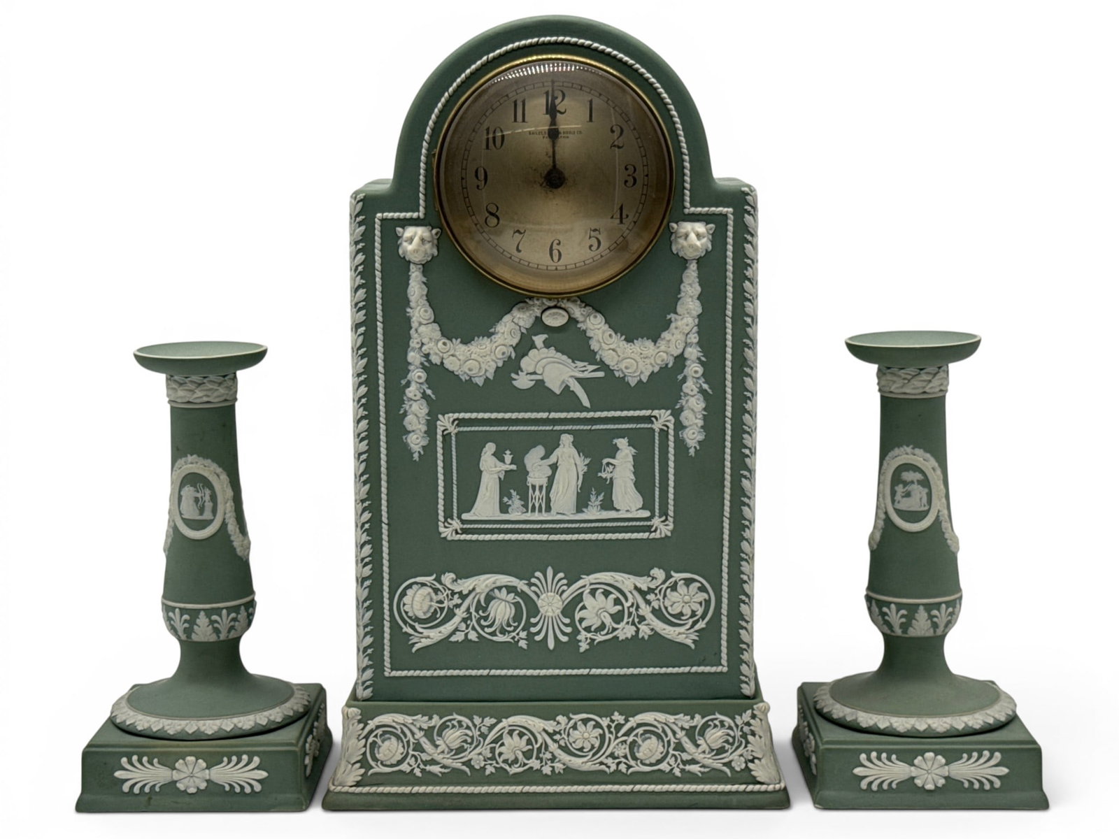 Wedgwood Sage Green Jasperware Garniture Set: A Wedgwood sage green jasperware garniture set with a relief classical-decorated mantel clock and two candlesticks. Clock face is marked Bailey Banks & Biddle. Clock: 15-1/2in tall x 9in wide. | You h