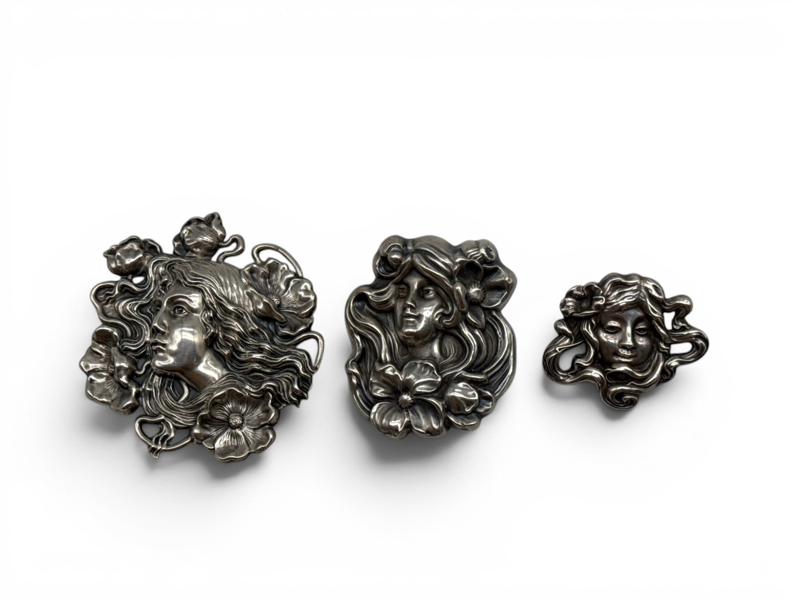 Three Sterling Silver Art Nouveau Face Brooches: Three sterling silver Art Nouveau stylized figural brooches decorated with botanical motifs. Each marked Sterling; the middle-sized brooch is marked Unger Brothers. Largest: 3in tall x 3in wide. Combi