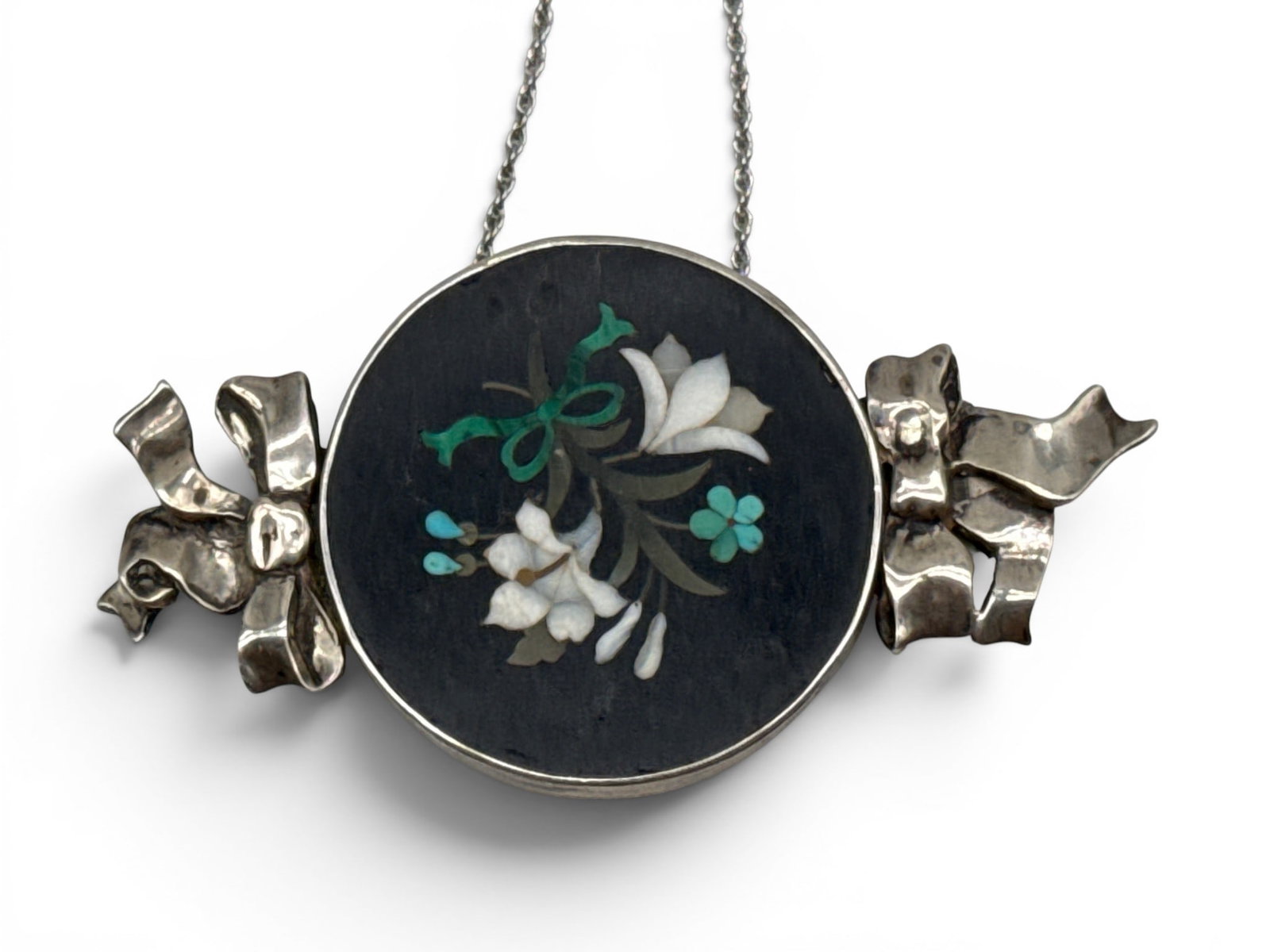 Silver Pietra-Dura Pendant Necklace: A floral pietra-dura inlaid pendant mounted in silver flanked by bow detail, on a sterling silver chain. Pendant: 1-3/4in tall x 3in wide. 24.2 dwt. | You have additional shipping options, and are not