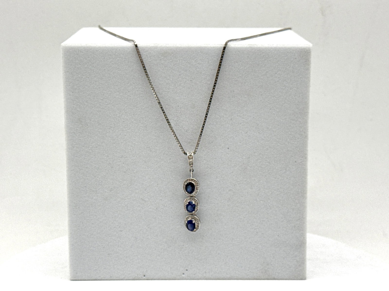 14K Sapphire and Diamond Necklace: A 14K white gold box chain necklace with pendant of three stacked sapphires each surrounded by diamonds. Chain is marked 14K. 18in long. Pendant: 1in long. 2.76 dwt. | You have additional shipping