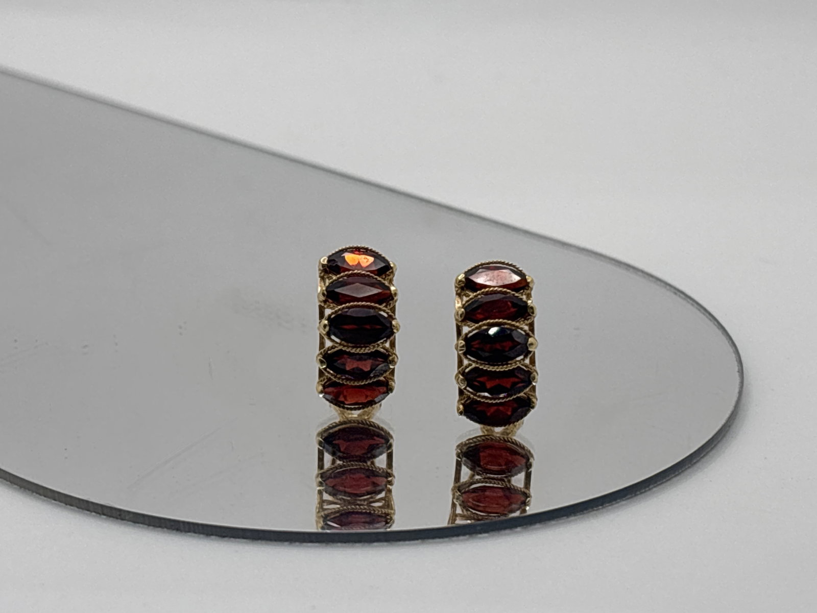 14K Stacked Marquis Cut Garnet Ear Clips: A pair of 14K yellow gold ear clips comprised of five 7.4mm x 3.5 mm east west set marquis-cut garnets in a semi-circular twist-textured surround. 3/4in tall. 2.95 dwt. | You have additional shipping 
