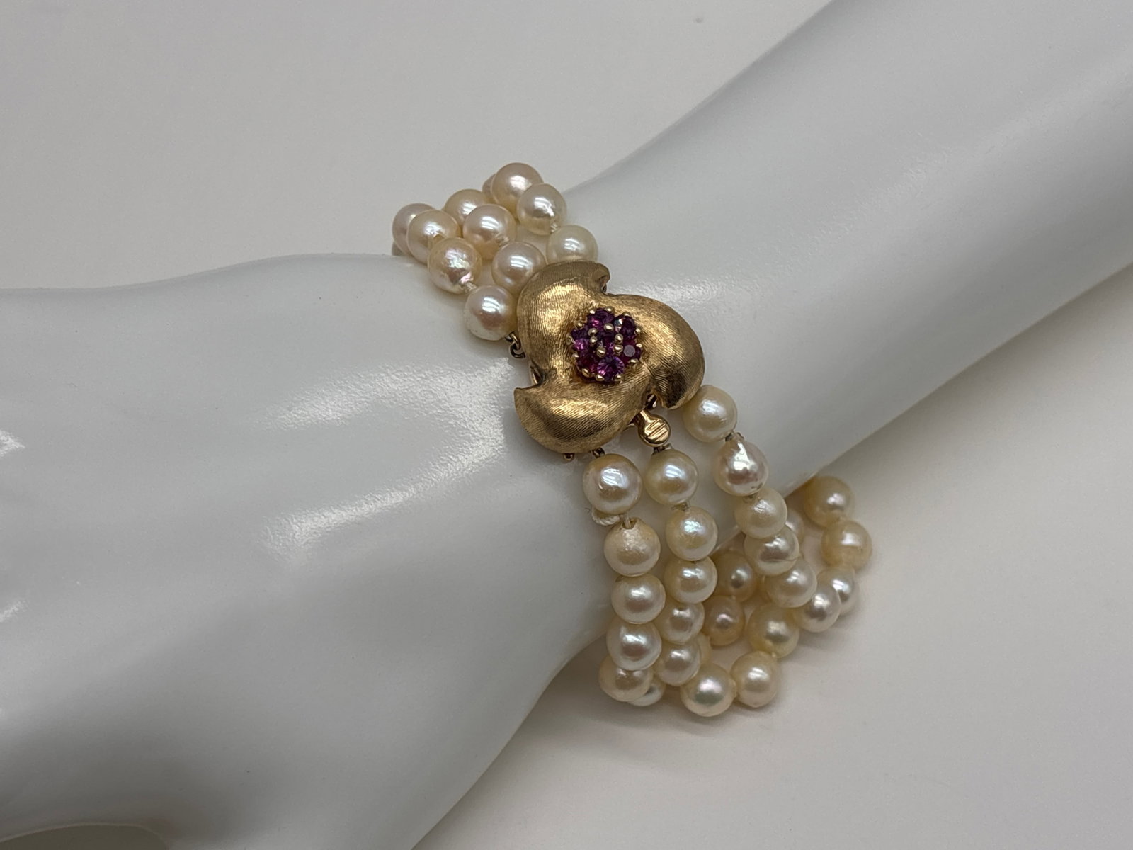 14K Three-Strand Pearl Bracelet with Ruby: A three-strand bracelet of 6.4 mm hand-knotted baroque pearls with a textured 14K clasp set with a ruby. Stamped 14K. 7-3/4in long. 21.44 dwt. | You have additional shipping options, and are not