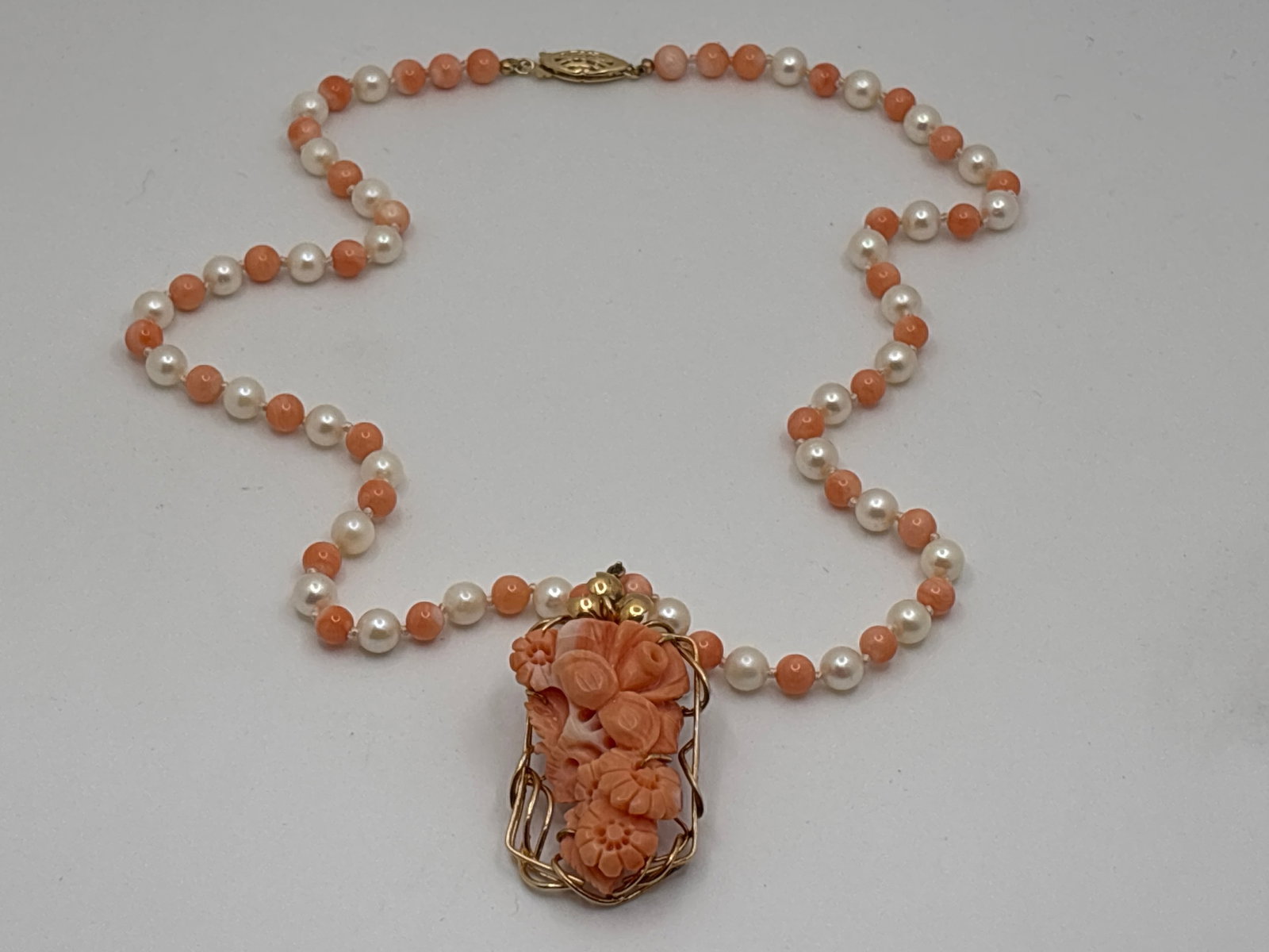 Carved Coral and Pearl Pendant Necklace: A 14K yellow gold set carved coral pendant of blooming floral form, suspended from a 5.5mm pearl and 4.8mm polished coral bead necklace. Closure and bale marked 14K. Pendant: 2-1/8in tall x 1in wide. 