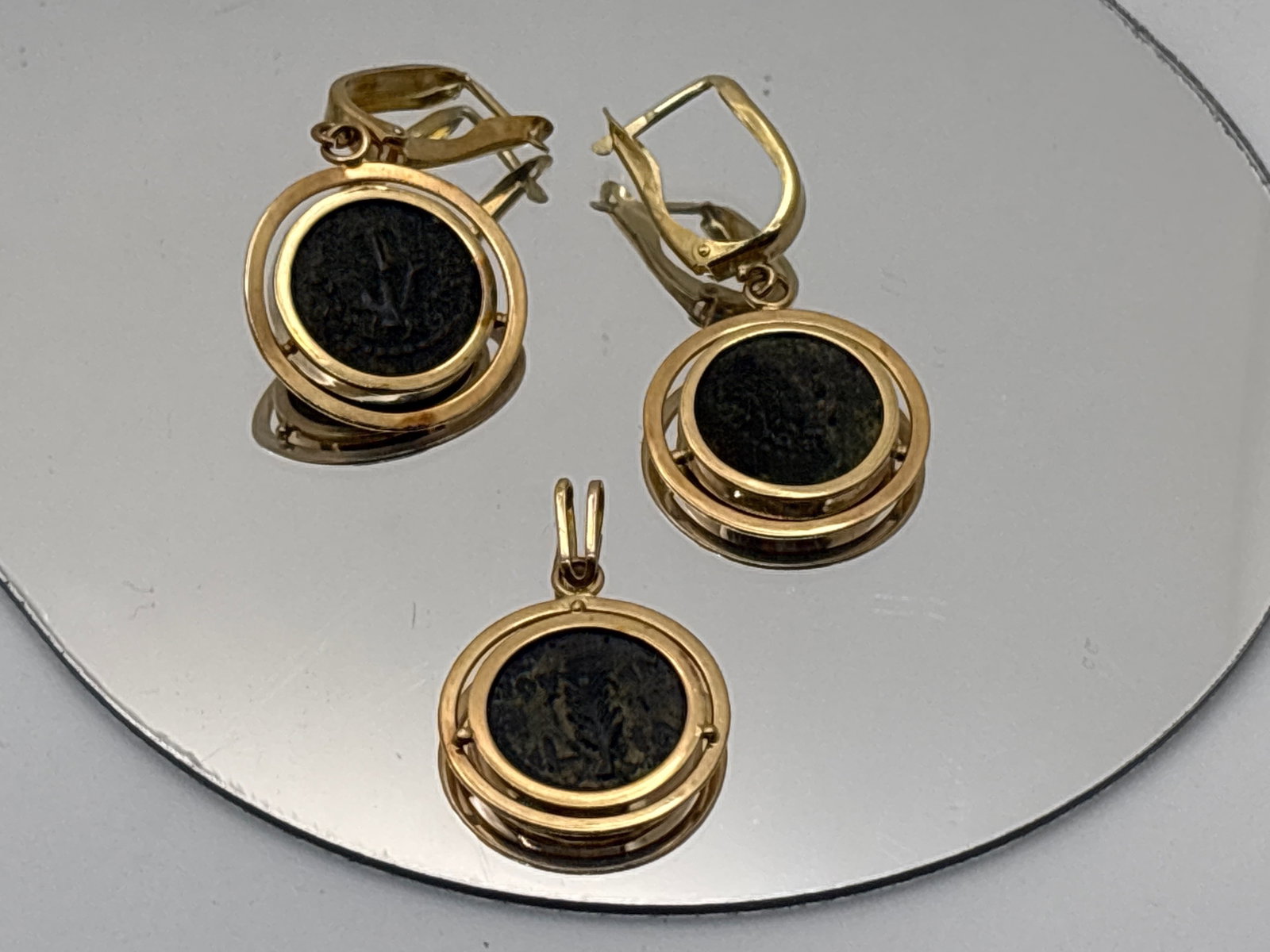 14K Masada Coin Pendant and Earring Suite: A pair of 14K (tested) yellow gold mounted Masada coins as drop earrings, and matching pendant, each in a bullseye surround. Pendant: 1-1/4in tall including bale. Earring: 1-5/8in long. 9.41dwt. |