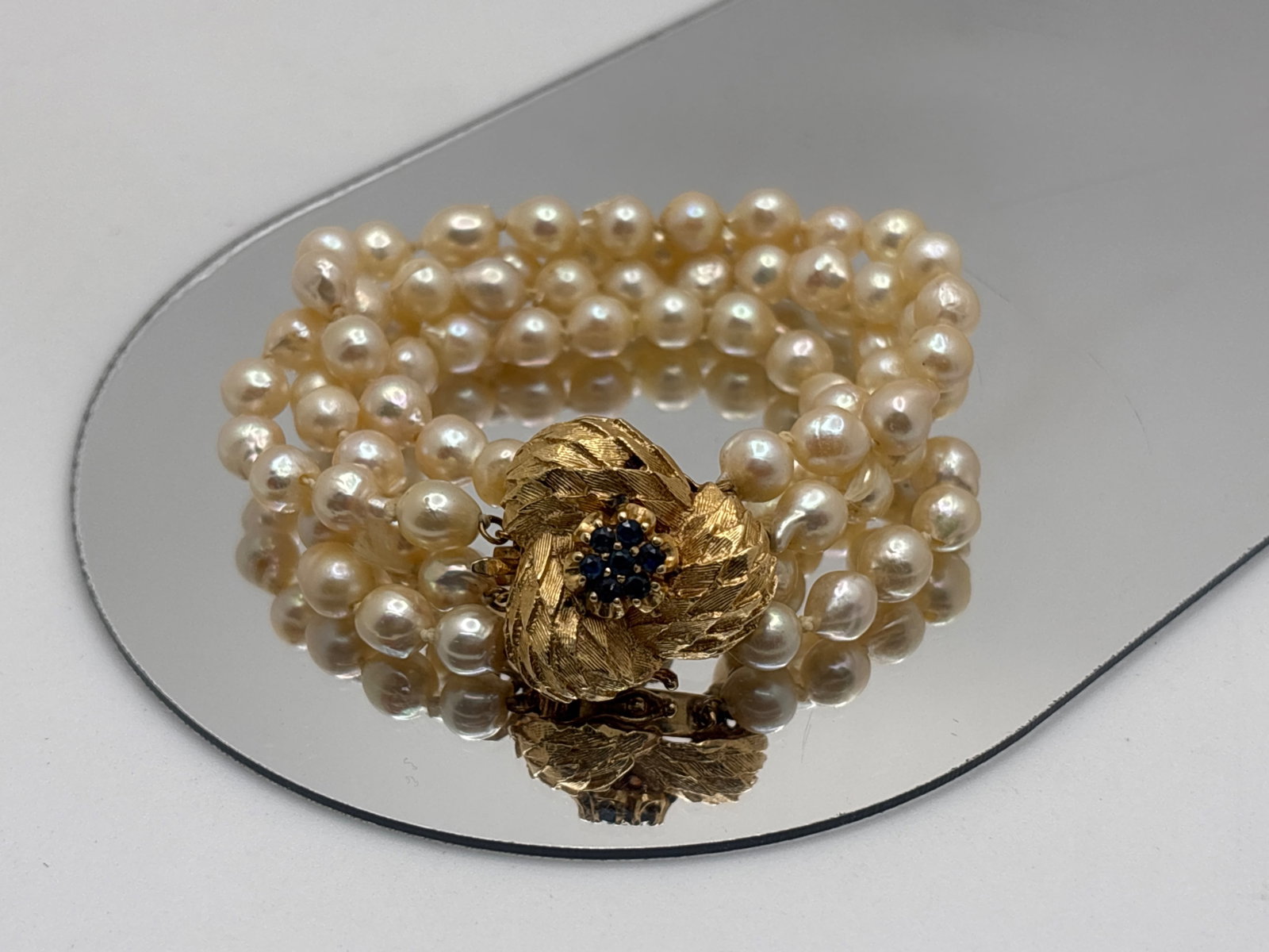 14K Yellow Gold and Sapphire Four-Strand Pearl Bracelet: A four-strand hand knotted baroque pearl bracelet with 6mm pearls and feather-textured clasp studded with seven 1.8mm sapphires. Stamped 14K. 6-5/8in long. 23.13 dwt. | You have additional shipping