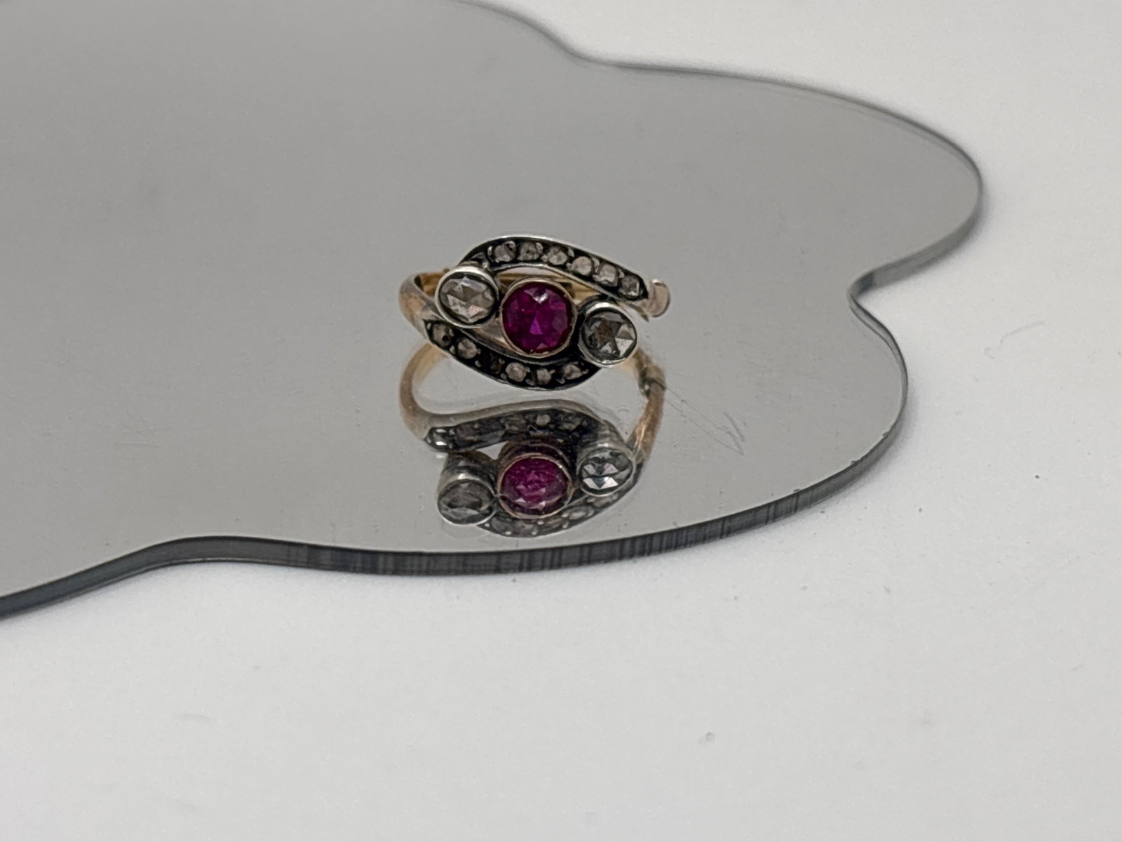 Belle Epoque 14K Ruby and Diamond Ring: A 14K yellow gold ring with a 4.2mm central bezel-set ruby flanked by bezel set 3mm rose cut diamonds, with twelve single cut flush-set diamonds curved above and below. Ring size 4.75/5, with sizer. 1