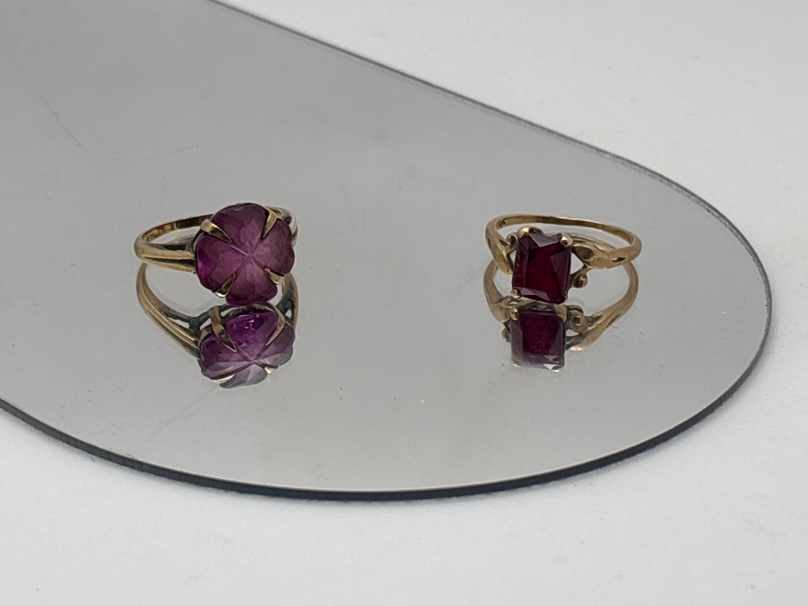 Two 10K Gold and Ruby Rings: Two 10K yellow gold rings to include one featuring a lobed flower-form ruby of 11.8mm at widest point; and one with an emerald cut 8mm x 6.4mm ruby in a pierced and stylized setting. Each ring size