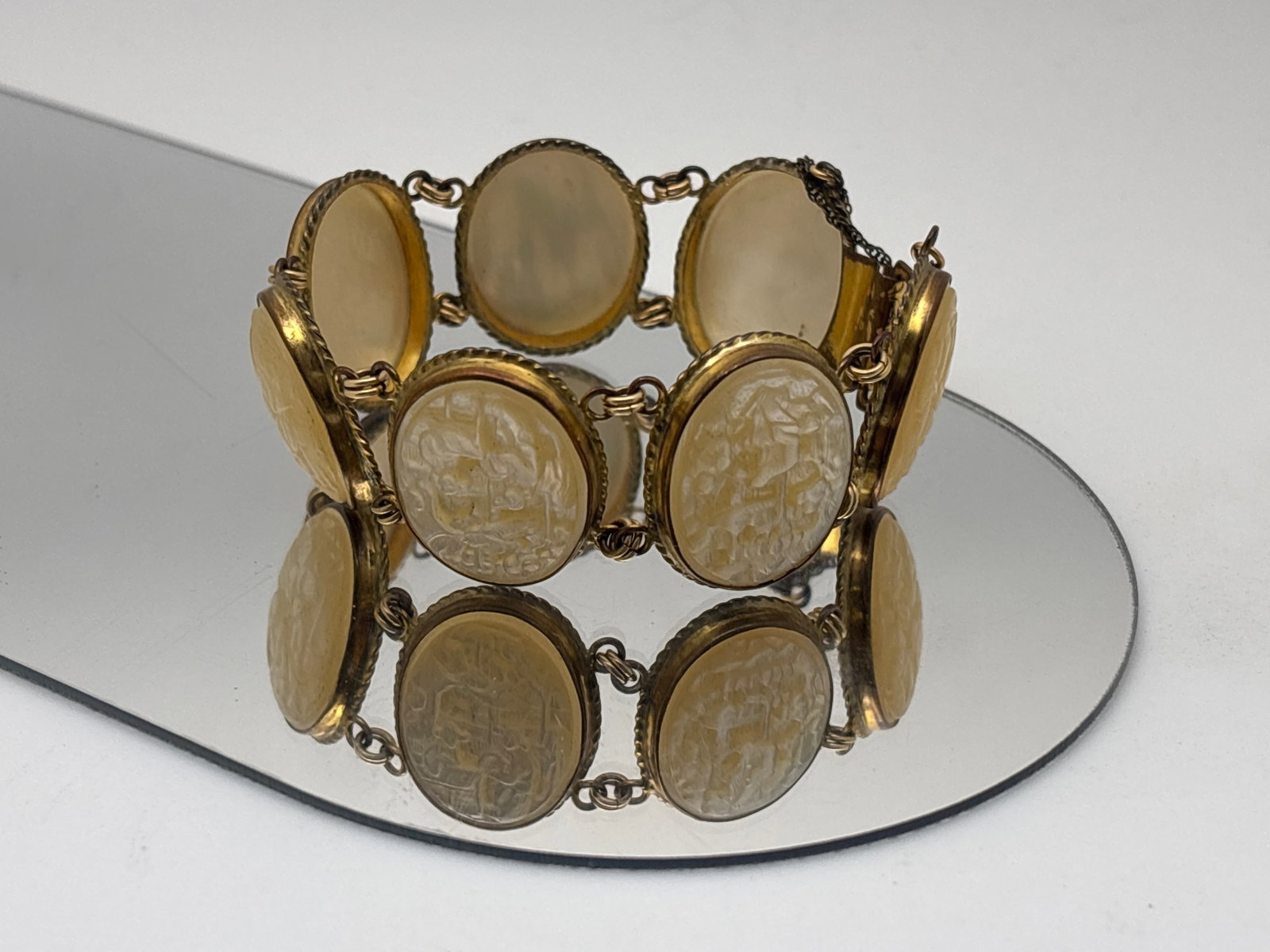 Mother of Pearl Carved Link Bracelet: A gold-filled mother of pearl disc link bracelet, featuring intricately carved figural and landscape decoration on each link. Links: 22mm x17.5mm. Bracelet: 7-1/8in long. | You have additional
