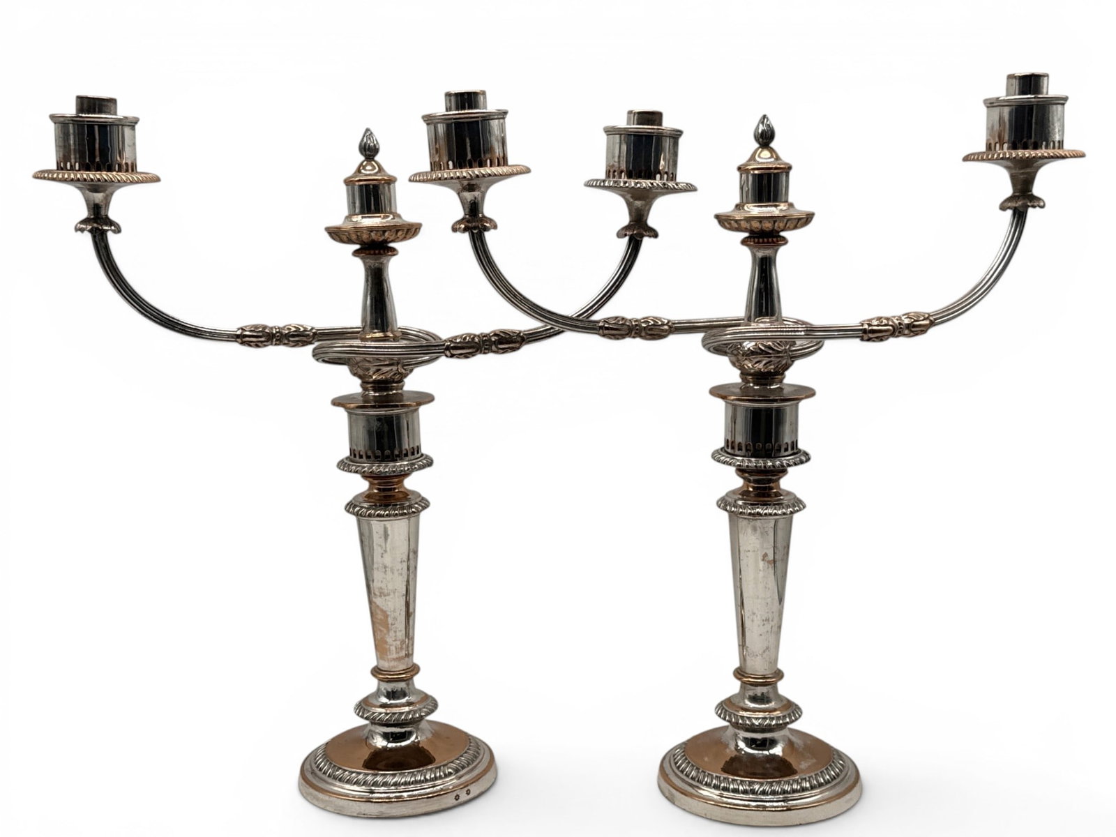 Matthew Boulton Sheffield Candlesticks: A pair of Matthew Boulton (English, 19th C.) for Sheffield silver plated copper two-arm candlesticks with gadrooned circular bases and tapering stems, laurel-decorated arms and flame finials. Hallmark