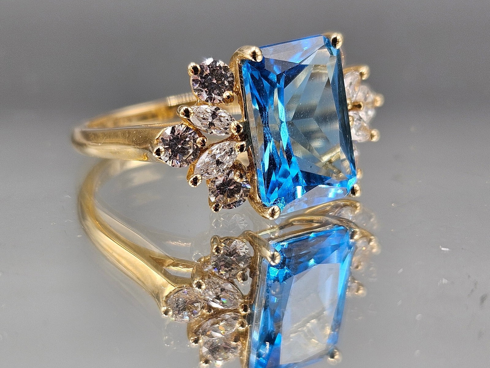 14K Ring with Emerald Cut Blue Topaz: A 14K yellow gold ring set with an emerald cut blue topaz flanked by cubic zirconia stones. Size 8. 2.63 dwt. | You have additional shipping options, and are not required to use Live Shipping. Additio