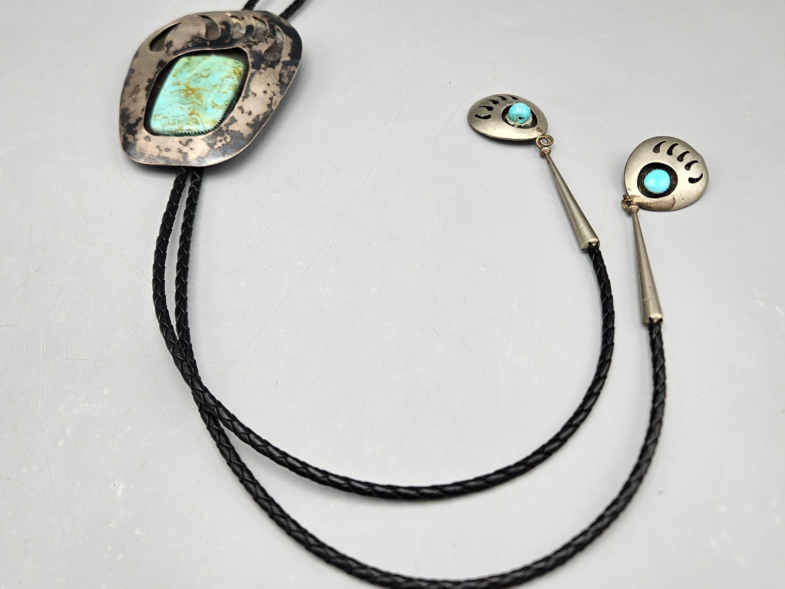 Hopi Silver and Turquoise Bear Claw Bolo Tie: A large Hopi silver bolo tie with bear paw set with a large turquoise stone at center, and two bear paw caps. Signed "J". 20in long x 3in wide. 40.10 dwt. | You have additional shipping options, and a