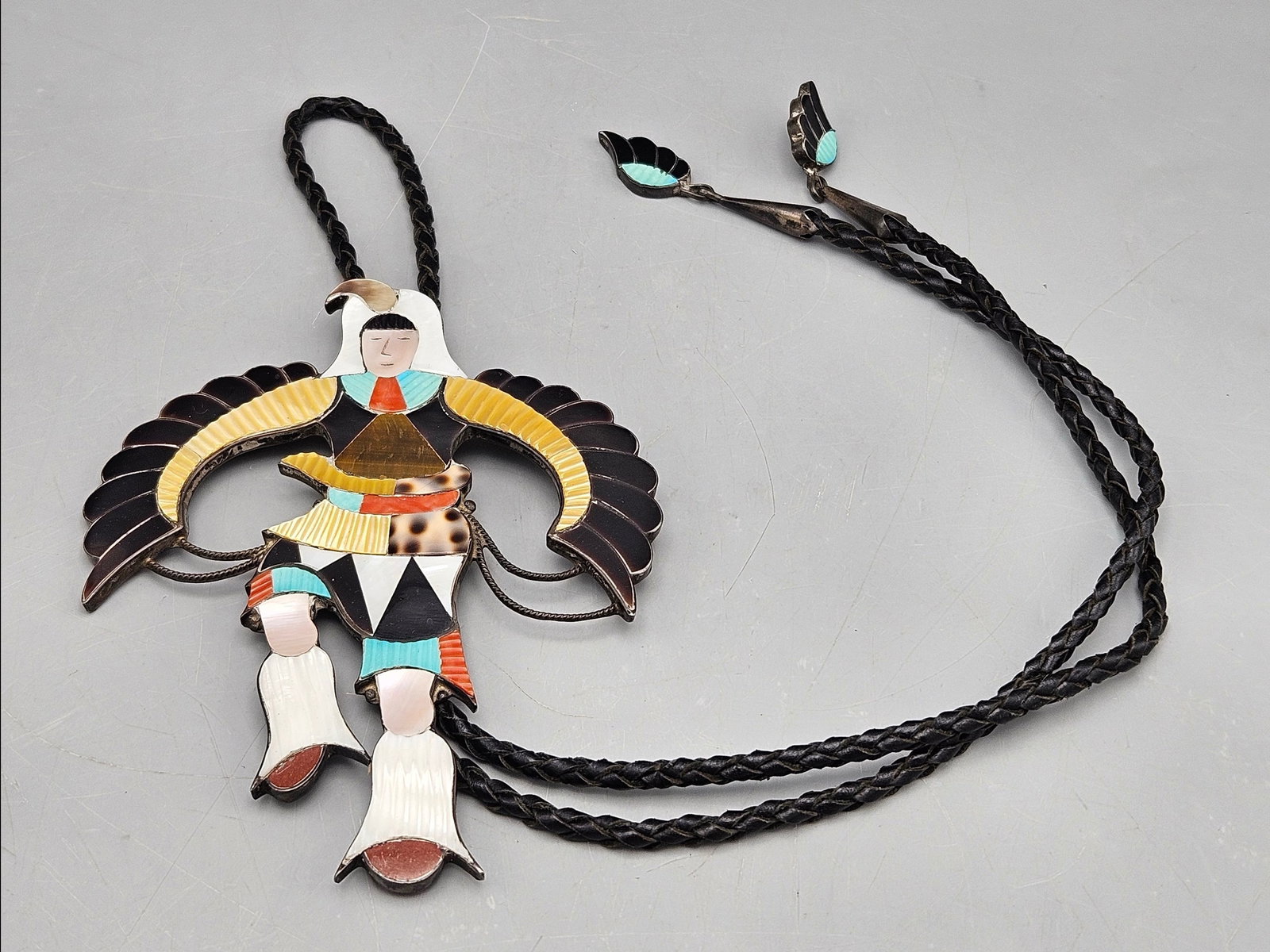 Jonathan Beyuka Zuni Eagle Dancer Bolo Toe: A Jonathan Beyuka (Zuni, 20th C.) silver-mounted bolo tie with inlaid turquoise, onyx, coral and mother of pearl depicting a dancing figure, with wing-form silver tips. Signed. 18in long. Figure: 5in 