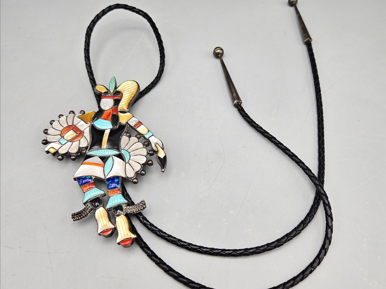 Zuni Sterling Silver Eagle Dancer Bolo Tie: A Zuni sterling silver bolo tie with mother of pearl, coral, turquoise, and onyx in an Eagle Dancer figure form. Marked sterling. 18in long. Figure: 5in tall x 3in wide. 45.5 dwt. | You have additiona