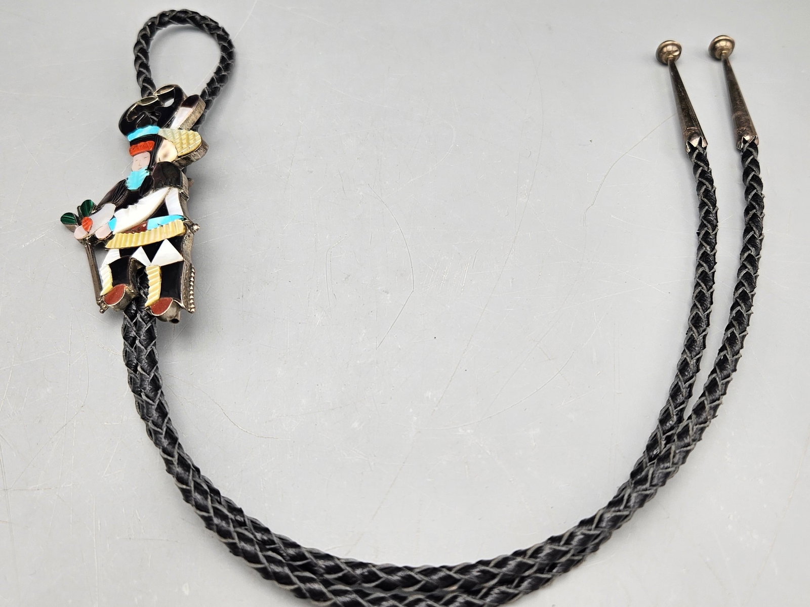 Edward Beyuka Zuni Dancer Bolo Tie: An Edward Beyuka (Zuni, 20th C.) bolo tie with Zuni silver ceremonial dancer figure slide set with malachite, coral, onyx, turquoise, and mother of pearl. Signed. 18in long. Figure: 4in long x 1-1/2in