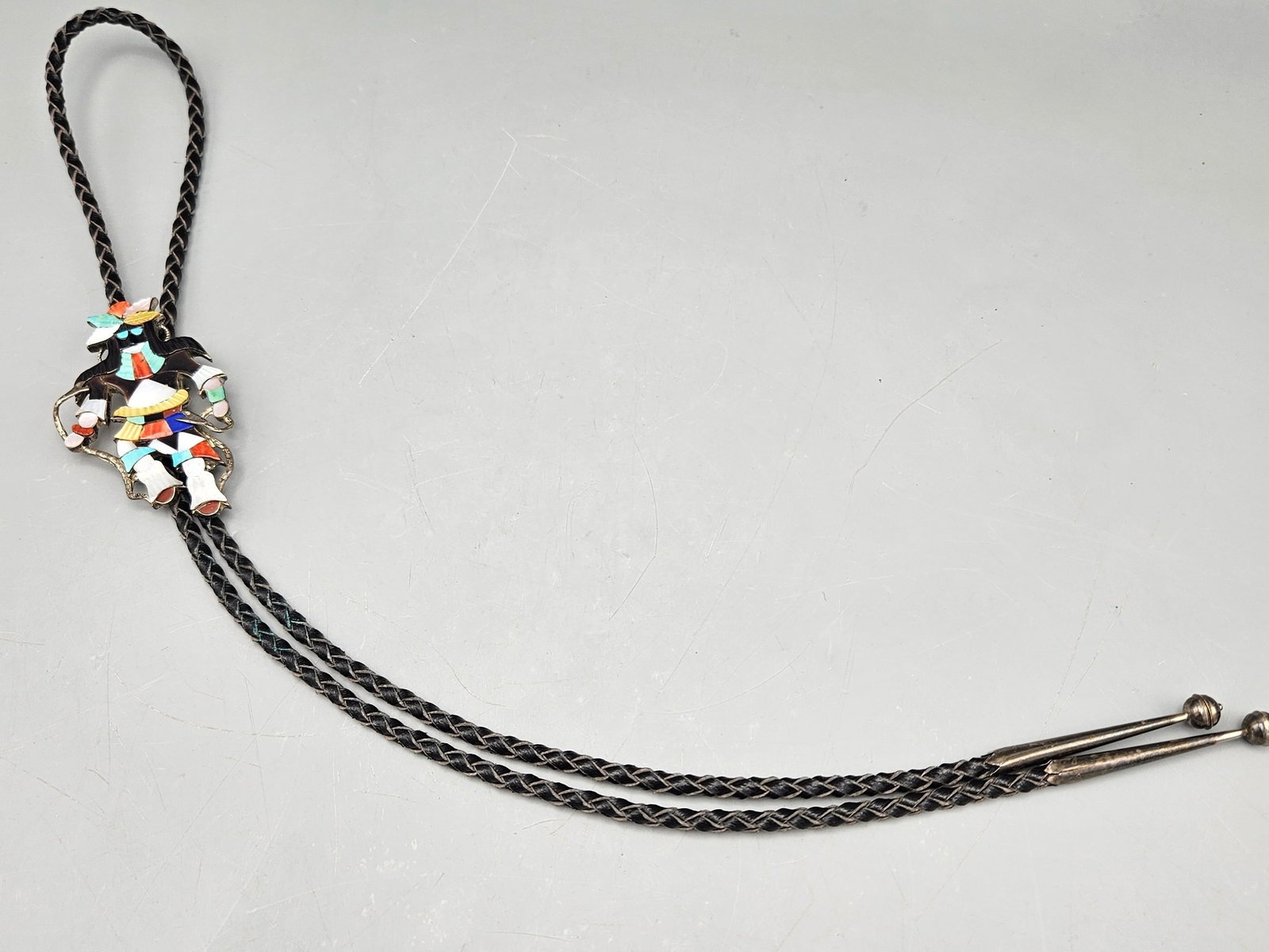 Beyuka Zuni Snake Dancer Bolo Tie: A Beyuka (Zuni, 20th C.) silver and inlaid stone bolo tie with snake dancer slide set with onyx, turquoise, coral, mother of pearl, and lapis. Signed. 18in long. Figure: 3in tall x 2in wide. 27.34 dwt