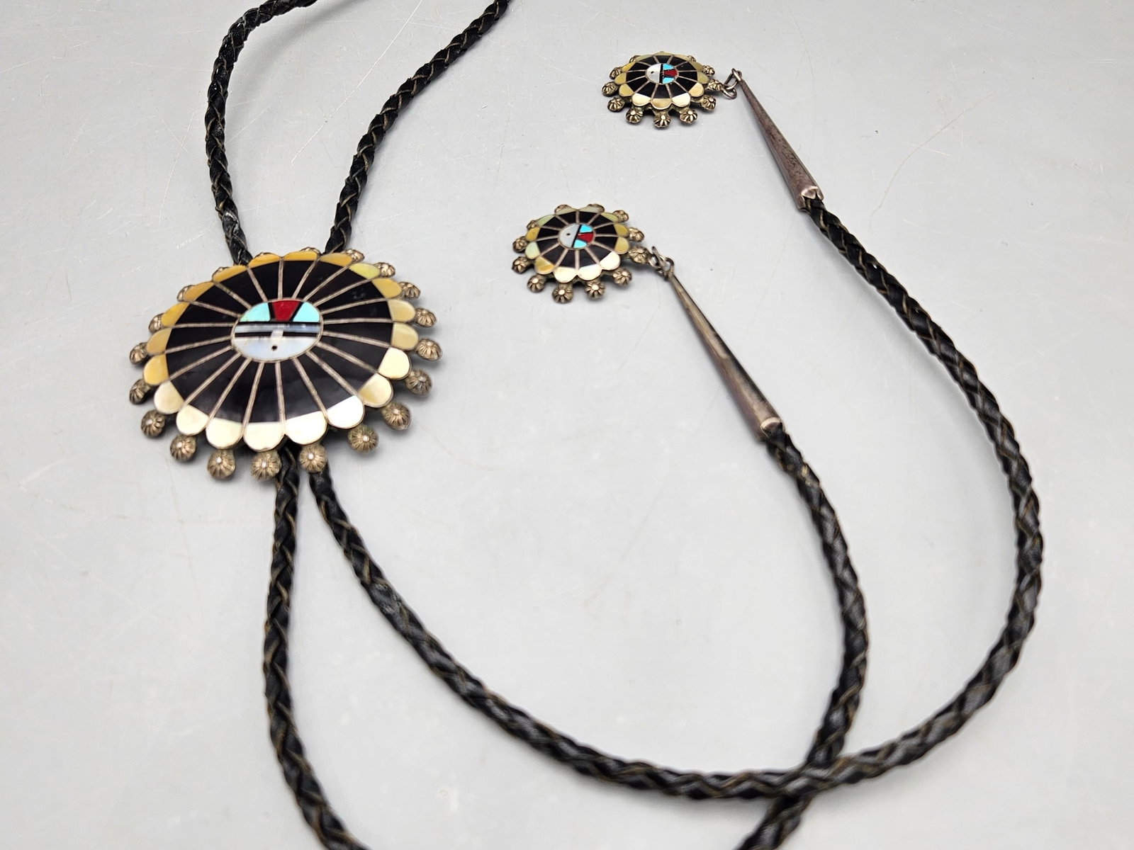 Zuni Silver Sunface Bolo Tie: A Zuni silver Sunface bolo tie and tie caps inlaid with onyx, turquoise, coral and mother of pearl. Signed. 21in long. Sunface: 2-1/2in tall x 2-1/2in wide. 36.45 dwt. | You have additional shipping o