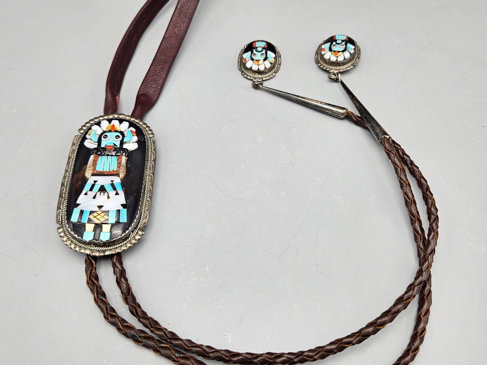 Beverly Estate Zuni Kachina Doll Bolo Tie: A Beverly Estate (Zuni, 20th C.) silver Zuni bolo tie with Kachina doll inlay on slide and tie caps. Signed. 21in long. Slide: 3in tall x 1-1/2in wide. 51.04 dwt. | You have additional shipping option