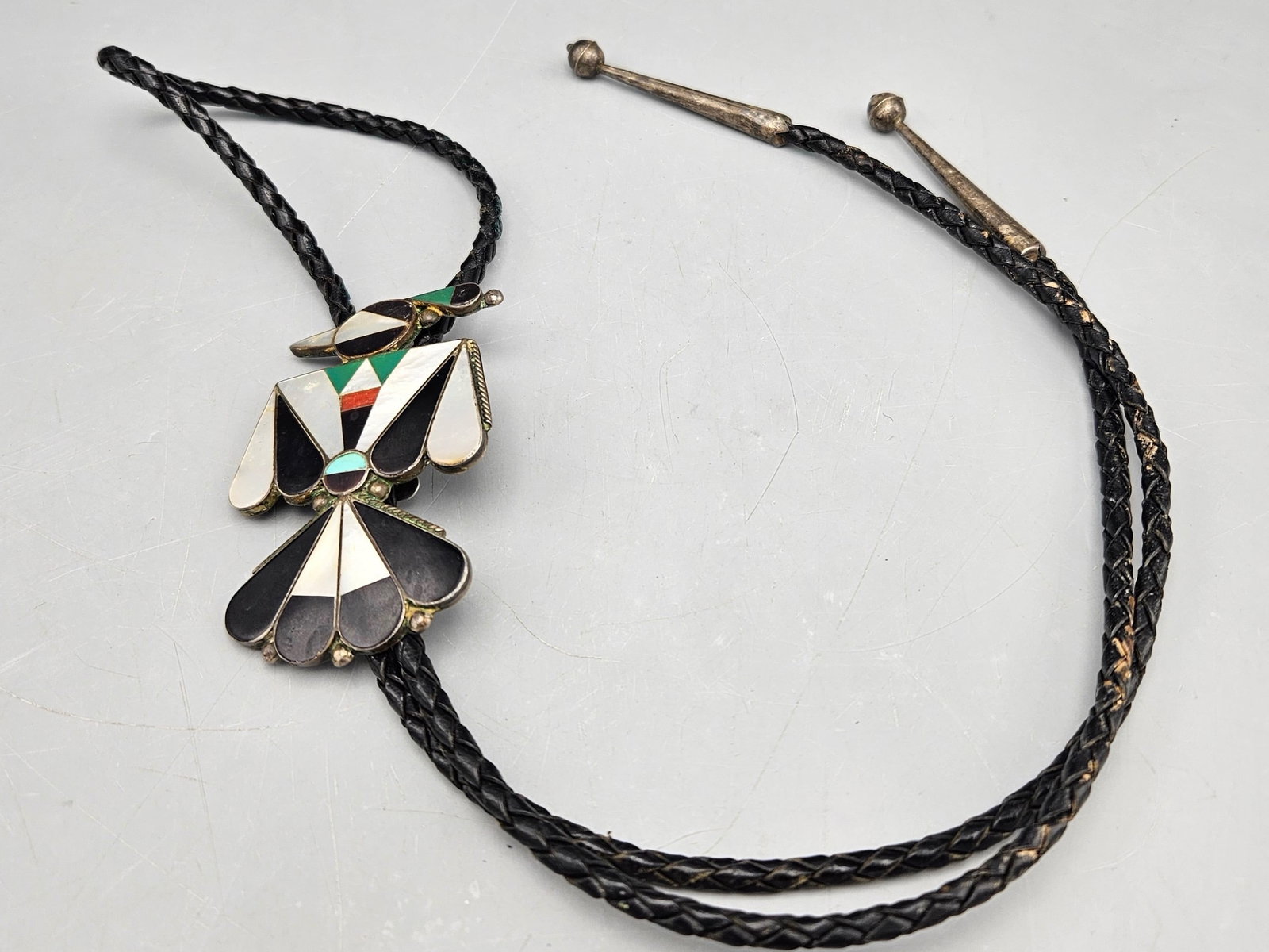 Lin Shebola Zuni Thunderbird Bolo Tie: A Lin Shebola (Zuni, 20th C.) silver bolo tie with thunderbird form with inlaid turquoise, onyx, coral, malachite and mother of pearl. Signed. 25.52 dwt. | You have additional shipping options, and ar