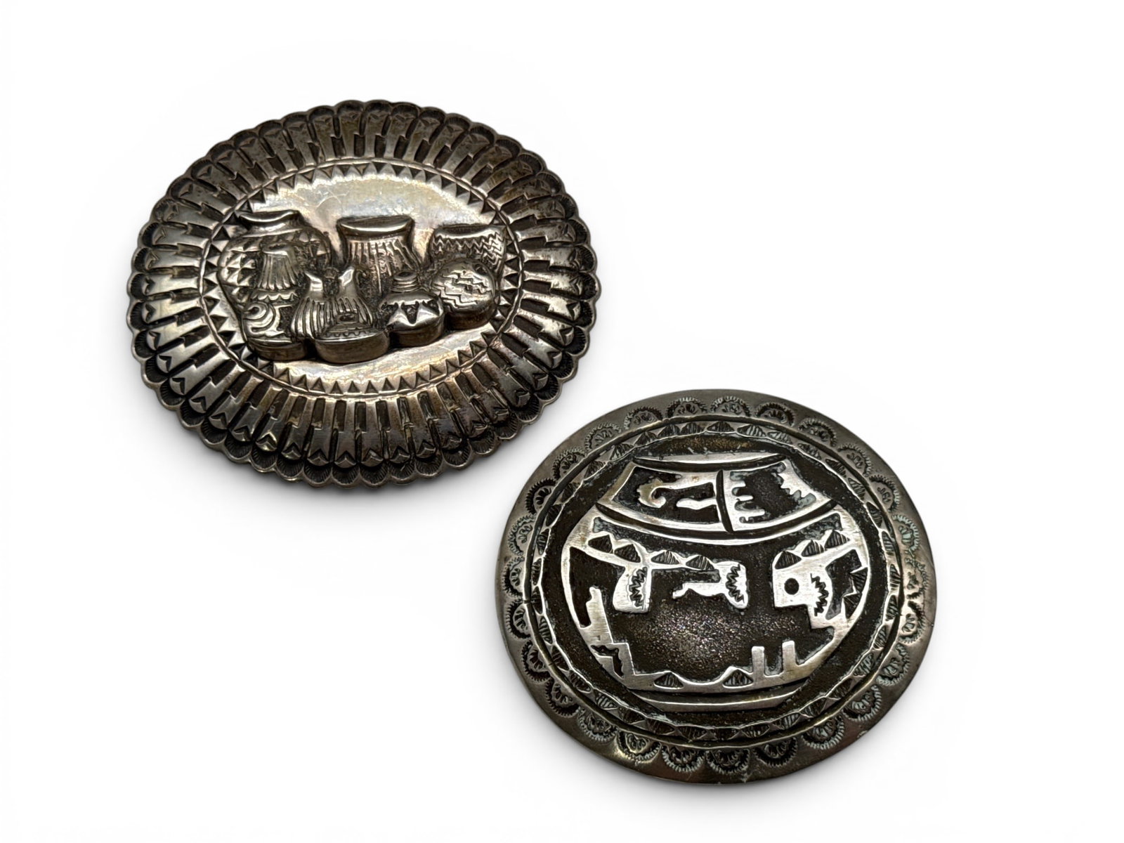 Two Navajo Sterling Acoma Relief Belt Buckles: To include a John Smith (Navajo, 20th C.) sterling silver belt buckle with Acoma pot relief, and a signed Navajo scalloped-edge belt buckle with high relief grouping of pottery. Each signed. Larger: 3