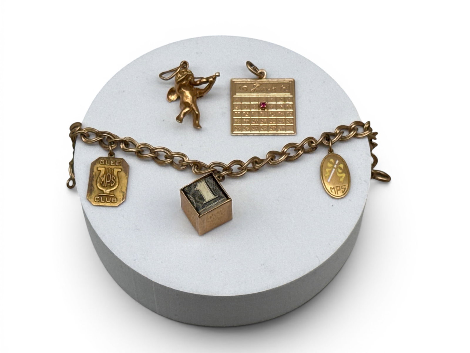 14K Yellow Gold Five-Charm Bracelet: A 14K yellow gold chain link bracelet with five 14K charms to include a cherub playing a violin, a birth month charm with ruby stone, a Glee club, a baton charm, and a "Mad Money" charm. Each marked 1