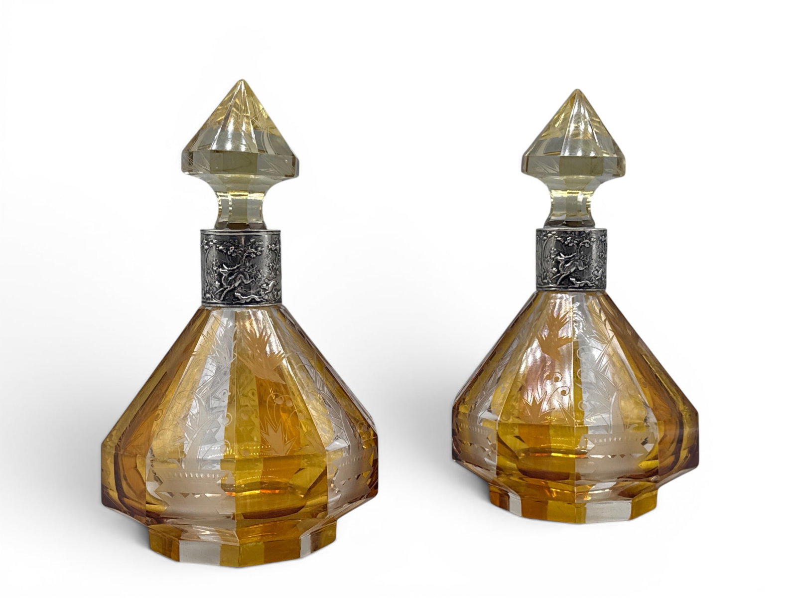 Pair Bohemian Crystal and German Silver Decanters: A pair of Bohemian crystal decanters with sliced cut neck design, alternating amber and clear panels decorated with stylized Art Deco engravings of diving swallows, diamond-form stoppers, and German .