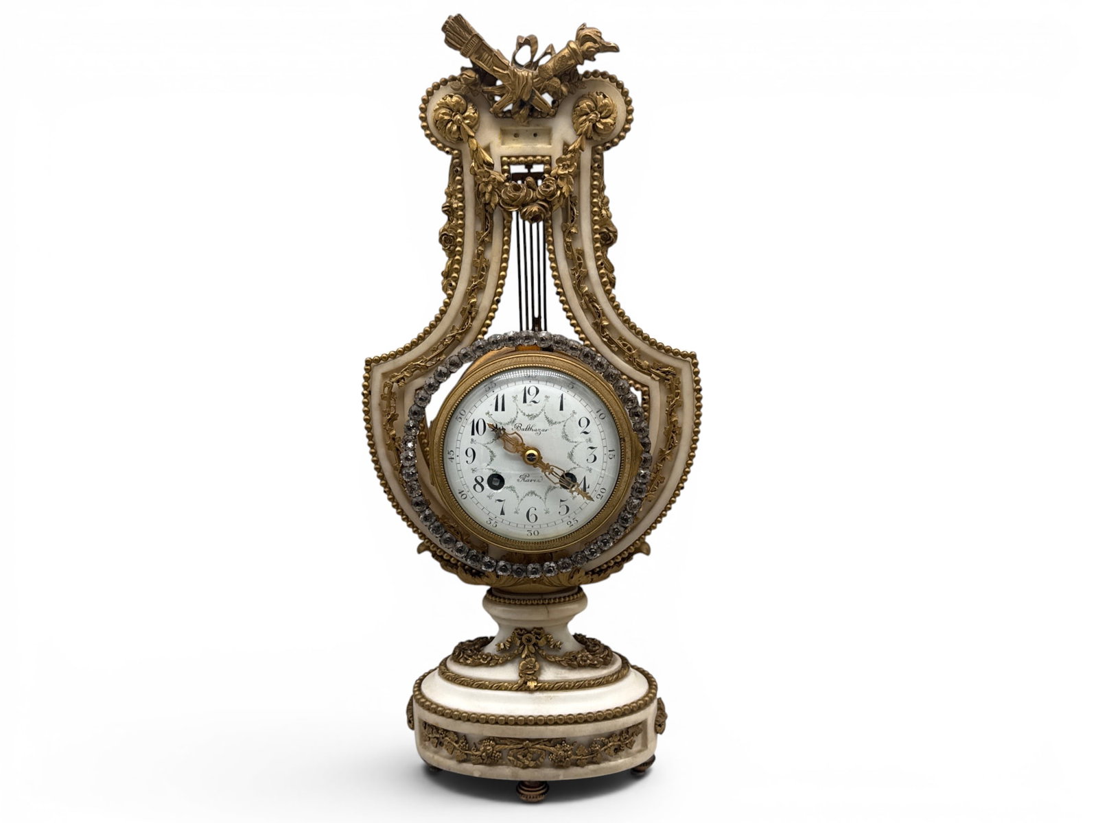 Louis XVI-Style Alabaster Lyre Clock: A French Louis XVI-style lyre-form alabaster mantel clock having a top surmounted with crossed torches supporting a floral festoon, and a paste jeweled bezel surrounding a patinated dial marked for Ba