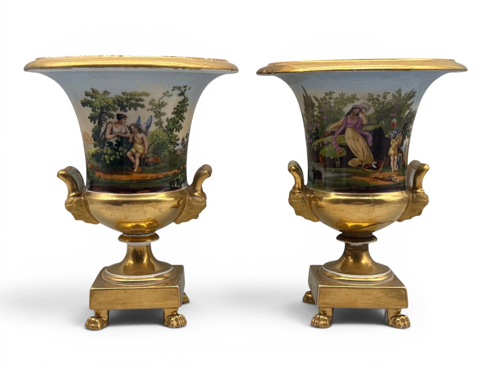 Pair of Paris Porcelain Campagna Urns: A pair of Paris porcelain Campagna urns with Neoclassical and landscape scenes, flanked by mask-form handles, terminating on gilt-decorated paw feet. 10in tall x 8in wide. Repair to base of one urn. |