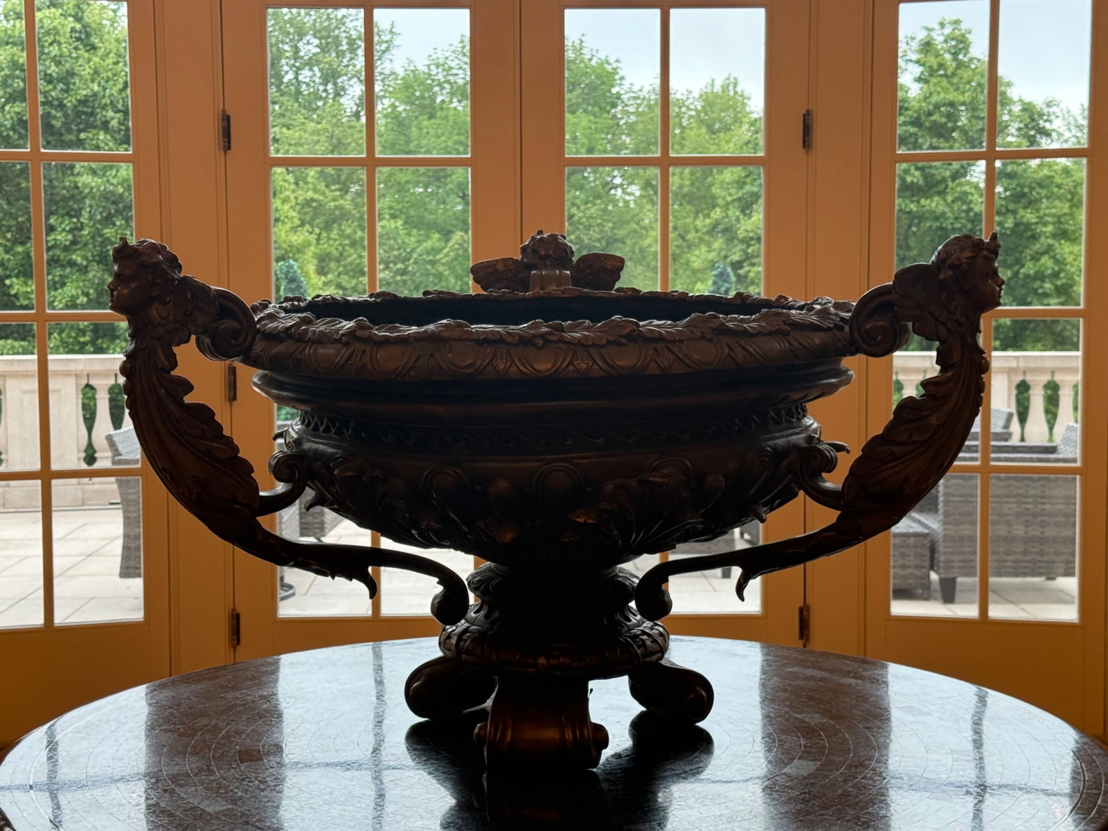 French-style Patinated Bronze Cherubic Centerpiece Bowl: A monumental French-style patinated bronze centerpiece bowl flanked by winged, cherubic figural handles with ornate, foliate design. | You have additional shipping options, and are not required to use