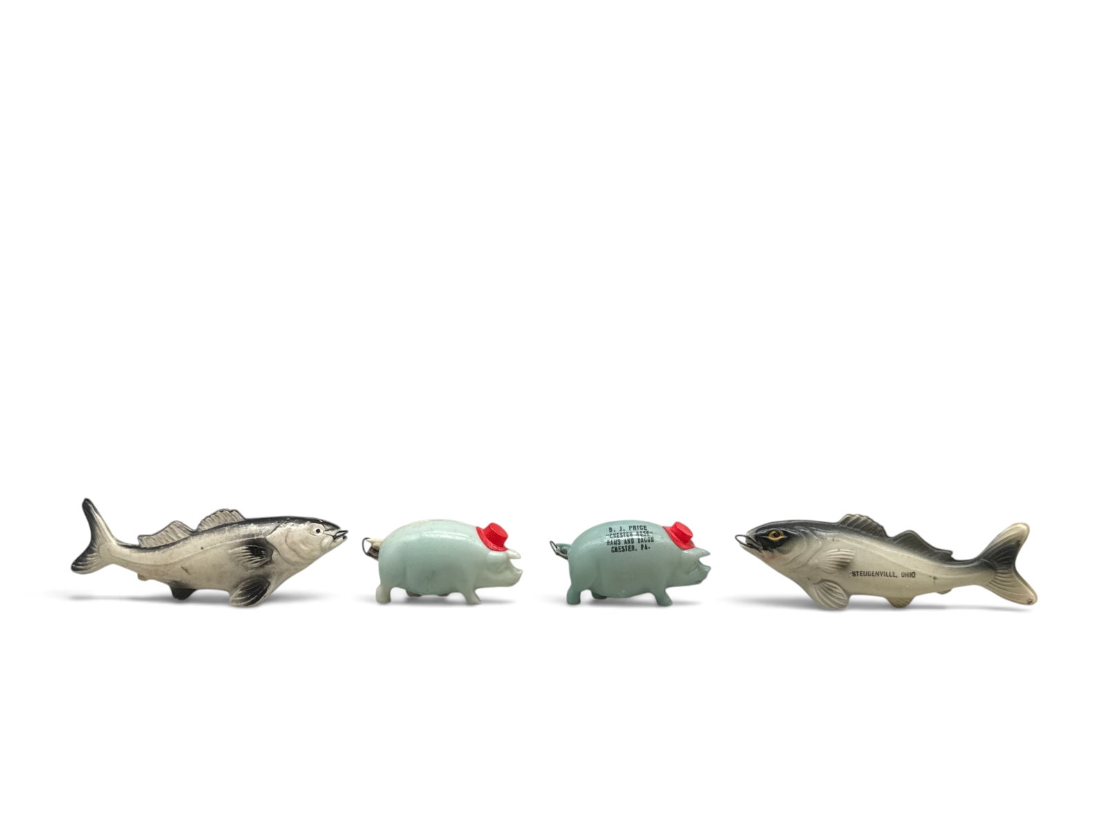 Four Celluloid Souvenir Tape Measures: Grouping to include an unmarked fish; unmarked pig; a pig with text "B.J. Price Chester Rose Hams and Bacon, Chester PA"; and a fish with "Steubenville, Ohio". Largest: 1-1/2in tall x 4in wide. | You
