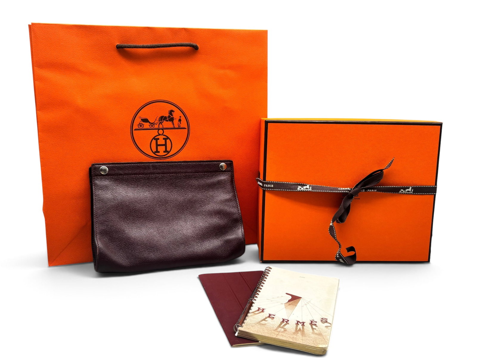 Hermes Karo Leather Purse: An Hermes Karo clutch purse in burgundy leather with snap closure. Marked Hermes on interior. Includes Hermes notebooks, gift box with ribbon and bag. 5in tall x 7-1/2in wide. | You have additional sh