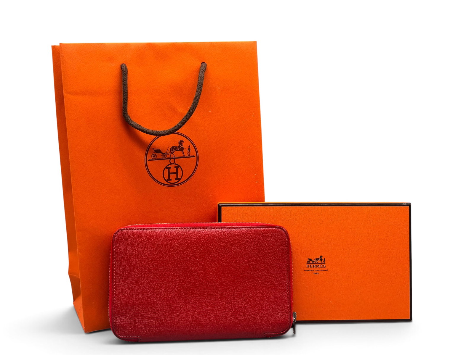 Hermes Azap Tourillon Clemence Wallet: An Hermes Azap Taurillon Clemence leather zip-around wallet in rouge with internal card slots, silver tone hardware, and Hermes address book. Marked Hermes on interior. Includes original Hermes box an
