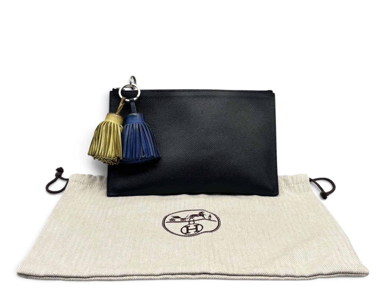 Hermes Leather Clutch and Two Carmen Tassel Rings: An Hermes Paris deep navy clutch with palladium zip closure, together with two Hermes carmen tassel key rings. Each marked Hermes. Includes Hermes dust cloth. 6in tall x 9in wide. | You have additiona