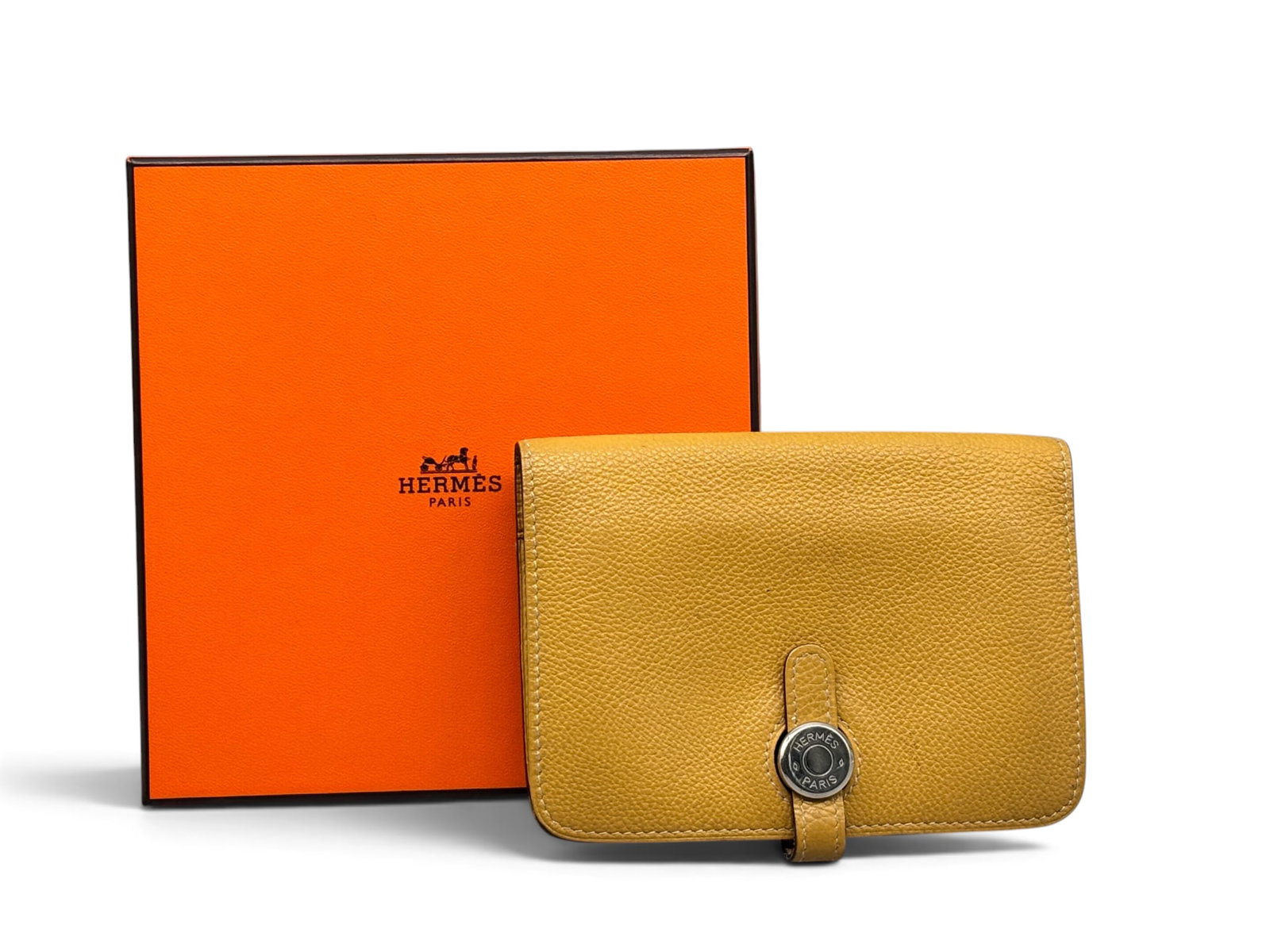 Hermes Curry Togo Calfskin Dogon Compact Wallet: An Hermes Paris Dogon compact wallet in 2C curry Togo leather with palladium hardware. Marked Hermes. Includes original Hermes box and receipt, circa 2012. 4in tall x 5-1/2in wide. | You have addition