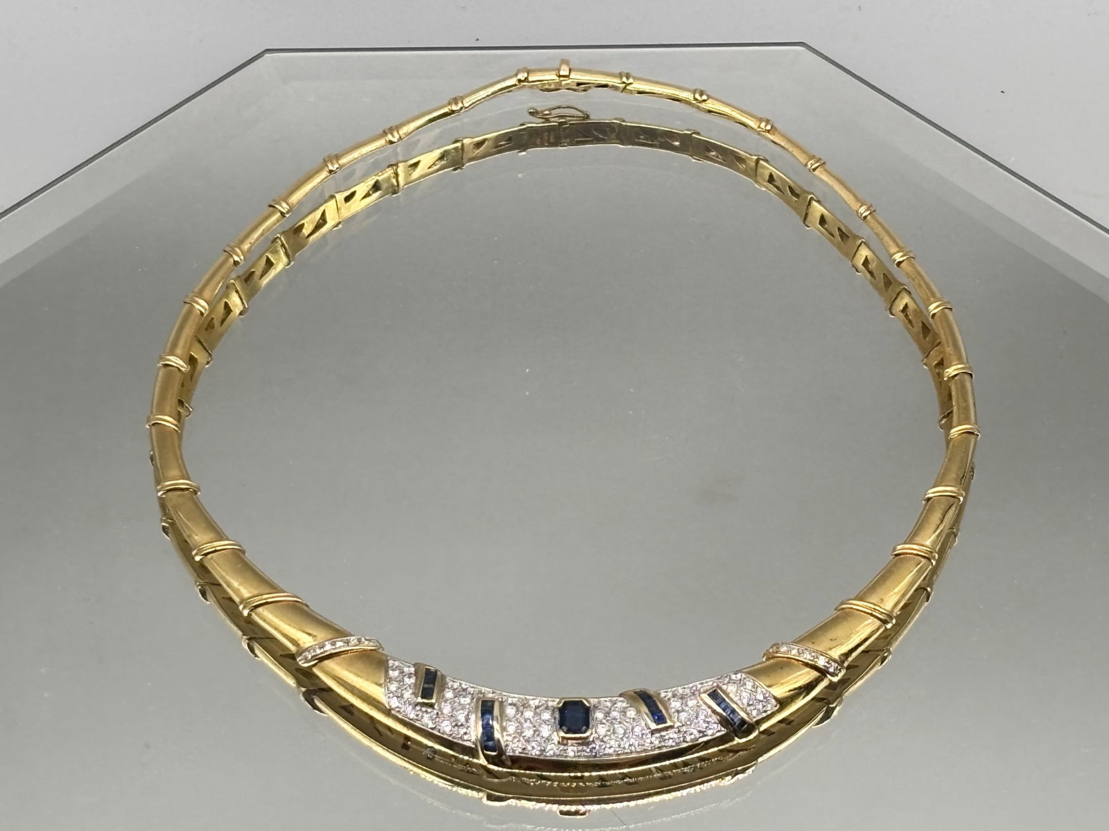18K Sapphire and Diamond Collar Necklace: An 18K yellow gold collar-form articulated necklace with center emerald cut sapphire surrounded by fifteen baguette cut sapphires and pave diamonds. Marked 750 on clasp. 55.1 dwt. | You have additiona