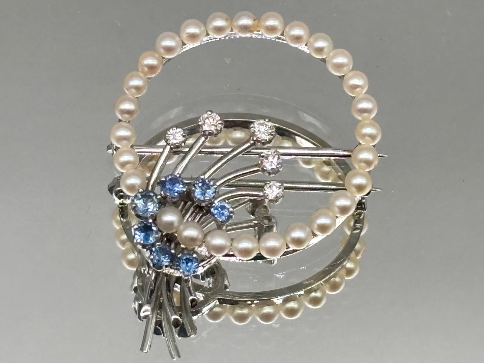14K Pearl, Diamond, and Blue Topaz Brooch: A circular 14K white gold and pearl brooch with a diamond and blue topaz spray motif. Marked 14K on clasp. 1in diameter. 3.72 dwt. | You have additional shipping options, and are not required to use L