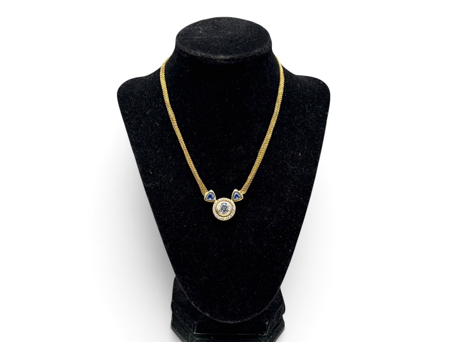 18K Sapphire, Diamond, and CZ Necklace: A 18K yellow gold multi chain necklace with a round cut cubic zirconium surrounded by a halo of diamonds flanked by two large sapphires. Necklace is marked 750 on clasp. Necklace is 14in long. 10.22 d