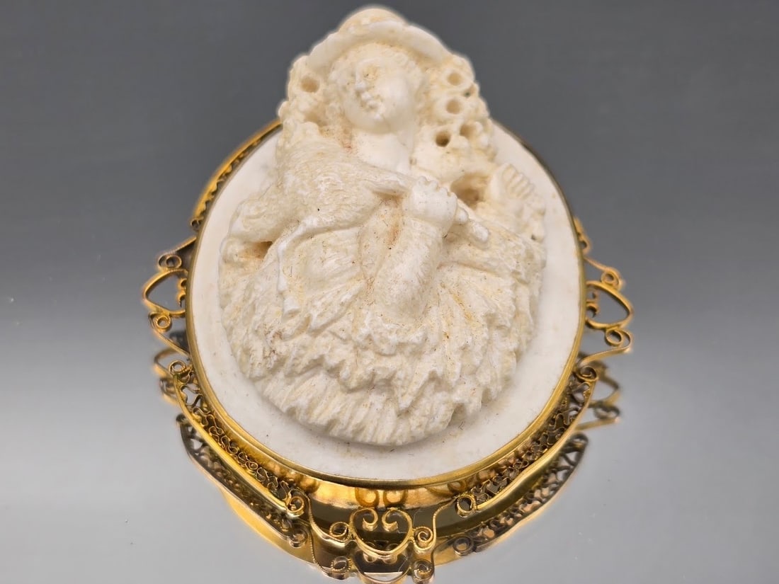 14K High Relief Figural Cameo Brooch: A 14K yellow gold mounted carved shell cameo depicting a woman with a lamb draped around her shoulders in high relief. Marked 14K. 2in tall x 1-1/2in wide. 19.41 dwt. | You have additional shipping op