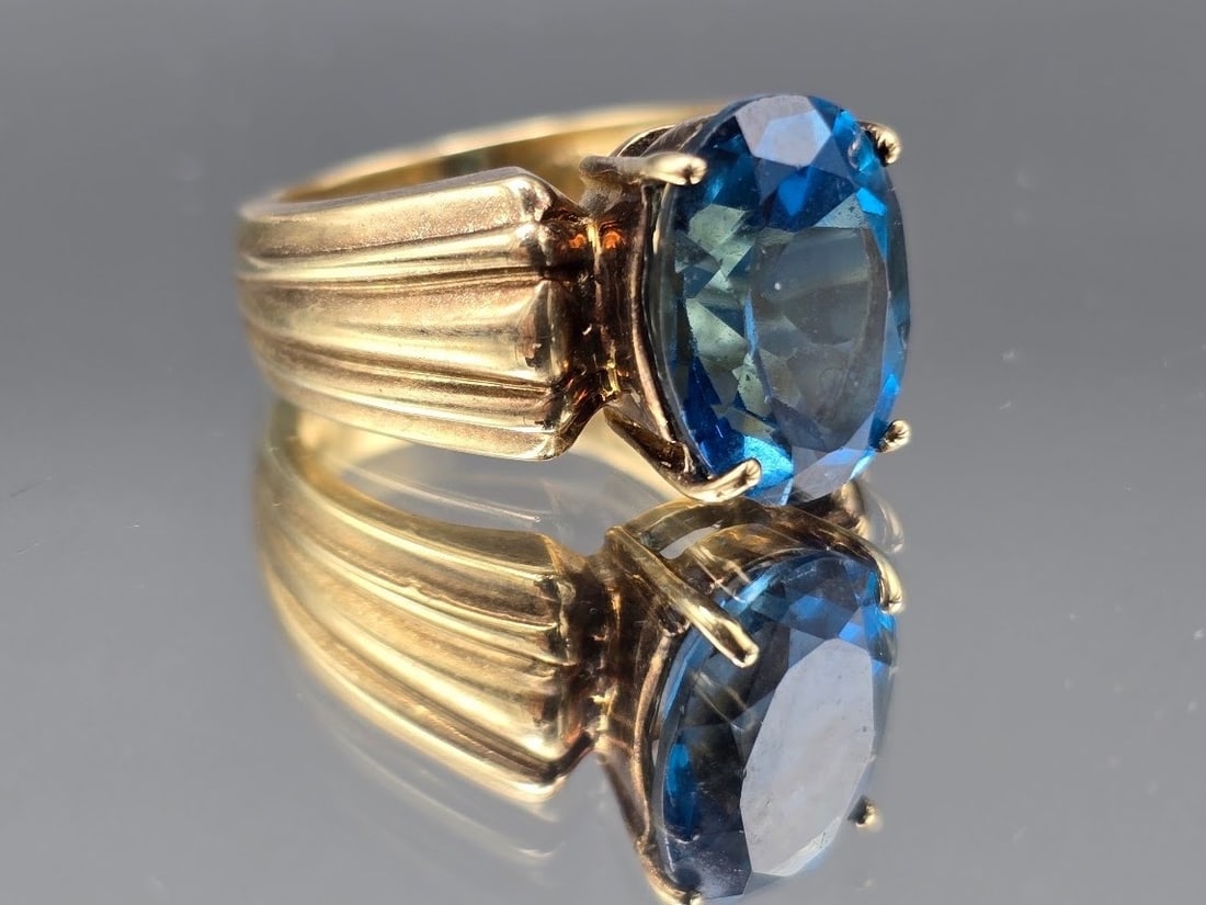 10K Oval Cut Blue Topaz Cocktail Ring: A 10K yellow gold ribbed-band cocktail ring with an oval cut blue topaz. Marked 10K. Size 7. 6.30 dwt. | You have additional shipping options, and are not required to use Live Shipping. Additional shi