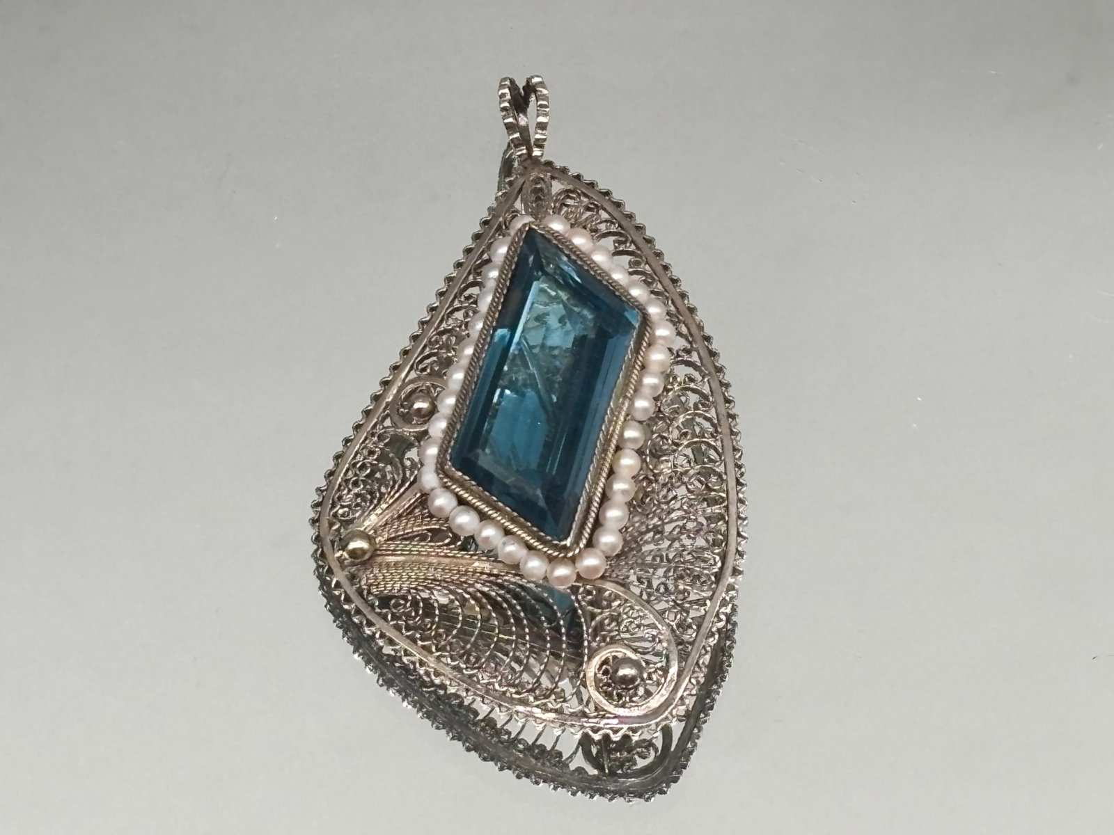 14K Blue Topaz and Pearl Filigree Pendant: A 14K white gold filigree pendant with a lozenge-cut 19ct blue topaz surrounded by a halo of pearls. Tests as 14K. 3in tall x 2in wide. 18.32 dwt. | You have additional shipping options, and are not r