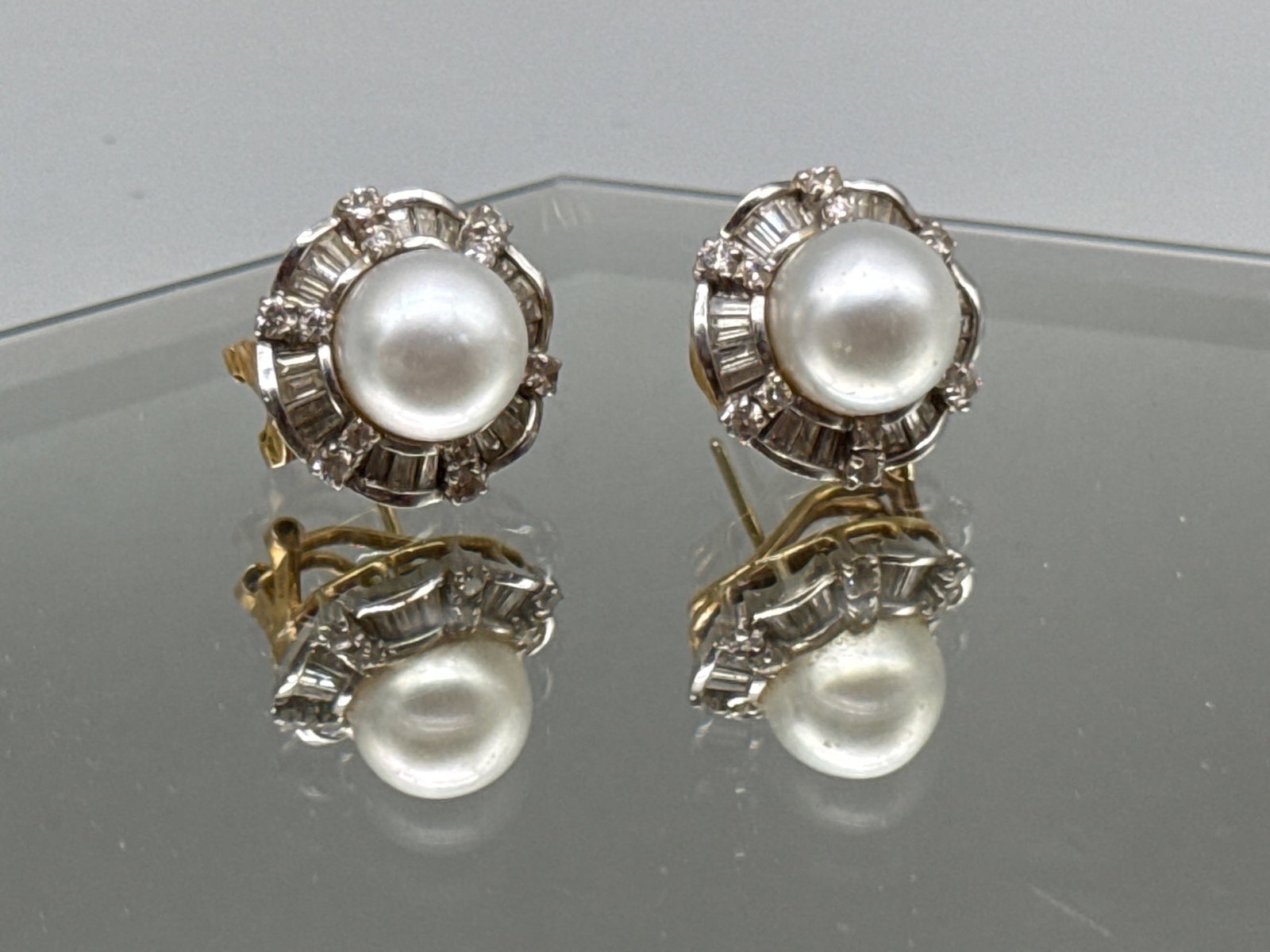 18K Diamond and Pearl Earrings: A pair of 18K white and yellow gold earrings with 11mm pearl surrounded by a halo of round and baguette cut diamonds. Marked 18K / 750 on clasp. 3/4in diameter. 11.18 dwt. | You have additional