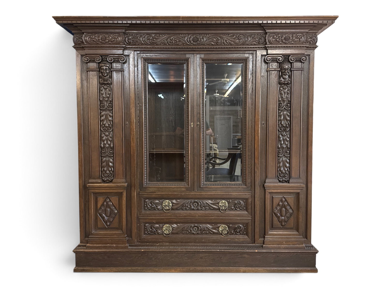 French Renaissance Revival Carved Cabinet: A French Renaissance Revival carved cabinet with an overhanding top over a case with two glass doors flanked by two cupboards with mask and foliate carving with columns, over two drawers. Breaks down 