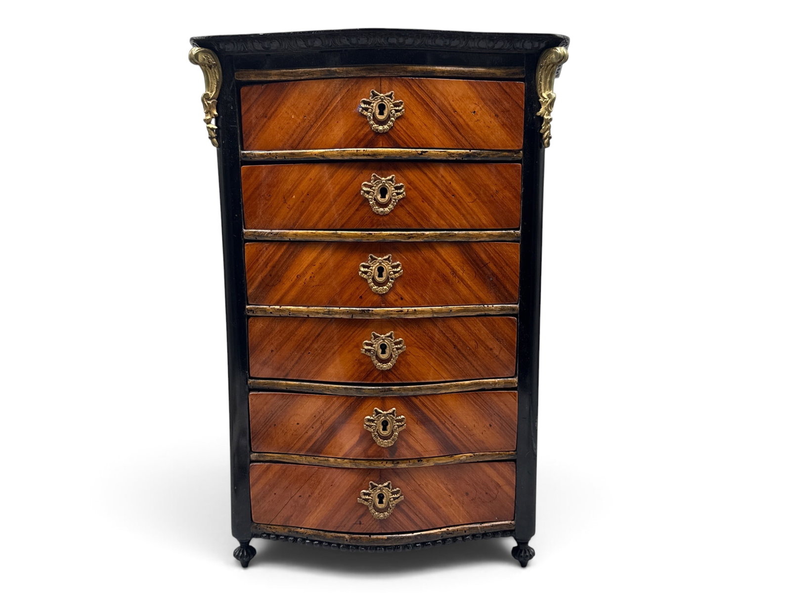 Napoleon III Gilt-Metal Miniature Chest: A Napoleon III gilt metal and wood veneered miniature chest of drawers with ebonized edges and ornate bow-decorated key holes, terminating on turned feet. 17in tall x 12in wide. | You have additional 