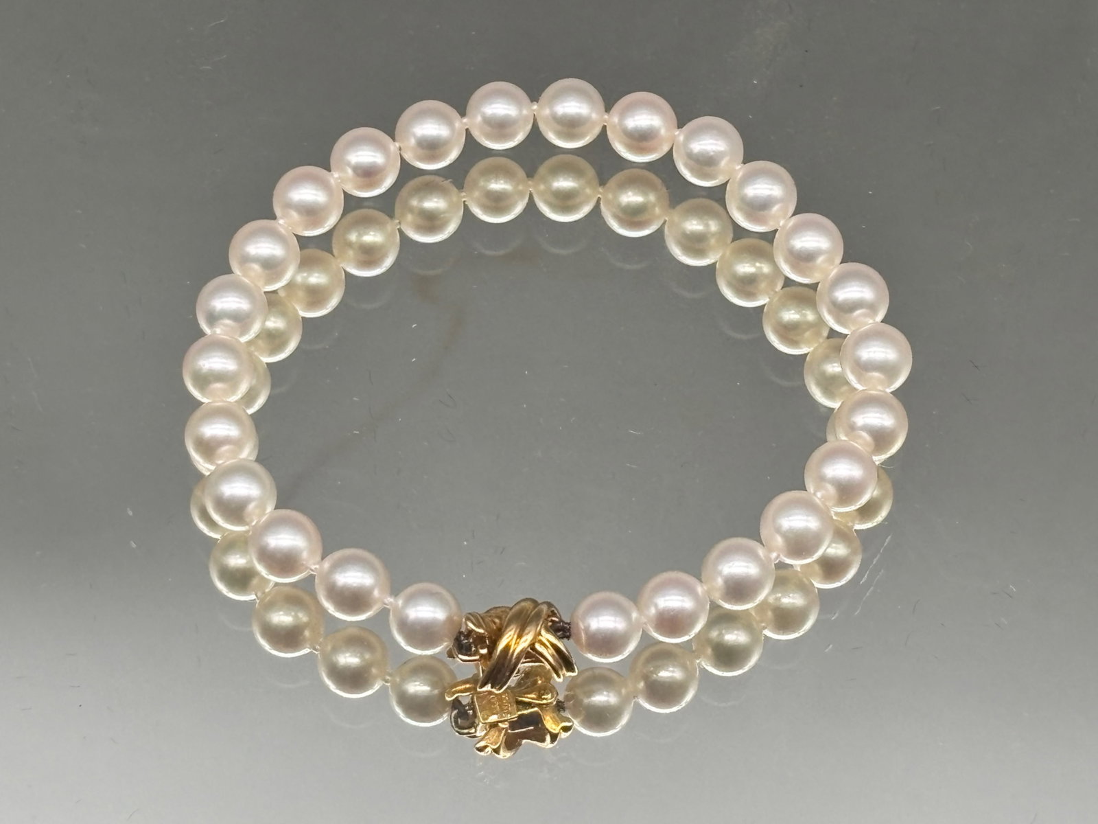 18K Tiffany & Co Hand-Knotted Pearl Bracelet: A Tiffany & Co. bracelet with 6mm hand-knotted pearls and an18K yellow gold knot clasp. Marked T&Co. / 18K on clasp. Includes Tiffany & Co. velvet-lined box. 6in long. 7 dwt. | You have additional shi