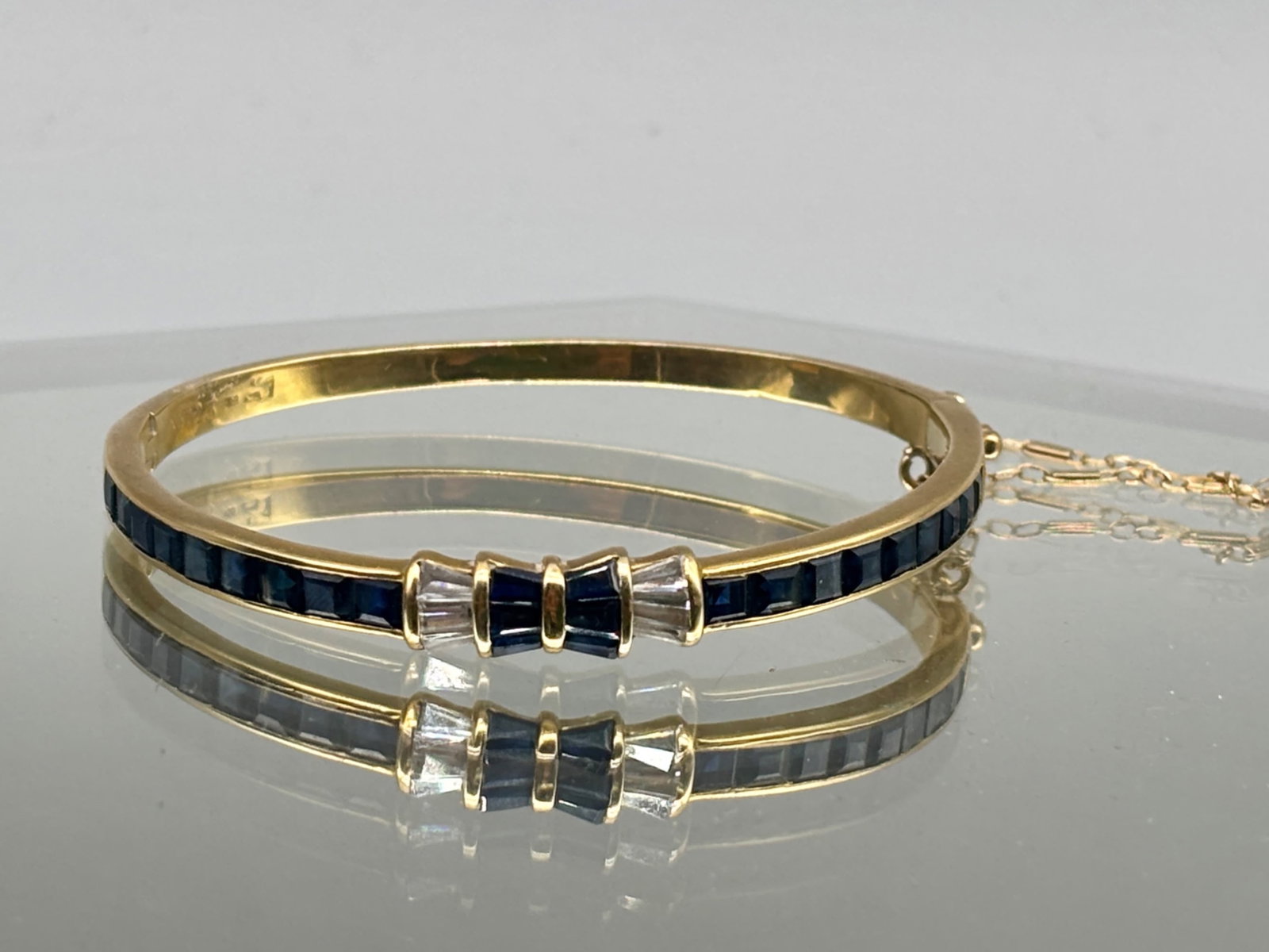 18K Art Deco-style Sapphire and Diamond Bracelet: A 18K yellow gold Art Deco-style bangle bracelet with channel-set sapphires and diamond baguettes at center. Tests as 18K. 2in diameter. 8.23 dwt. | You have additional shipping options, and are not