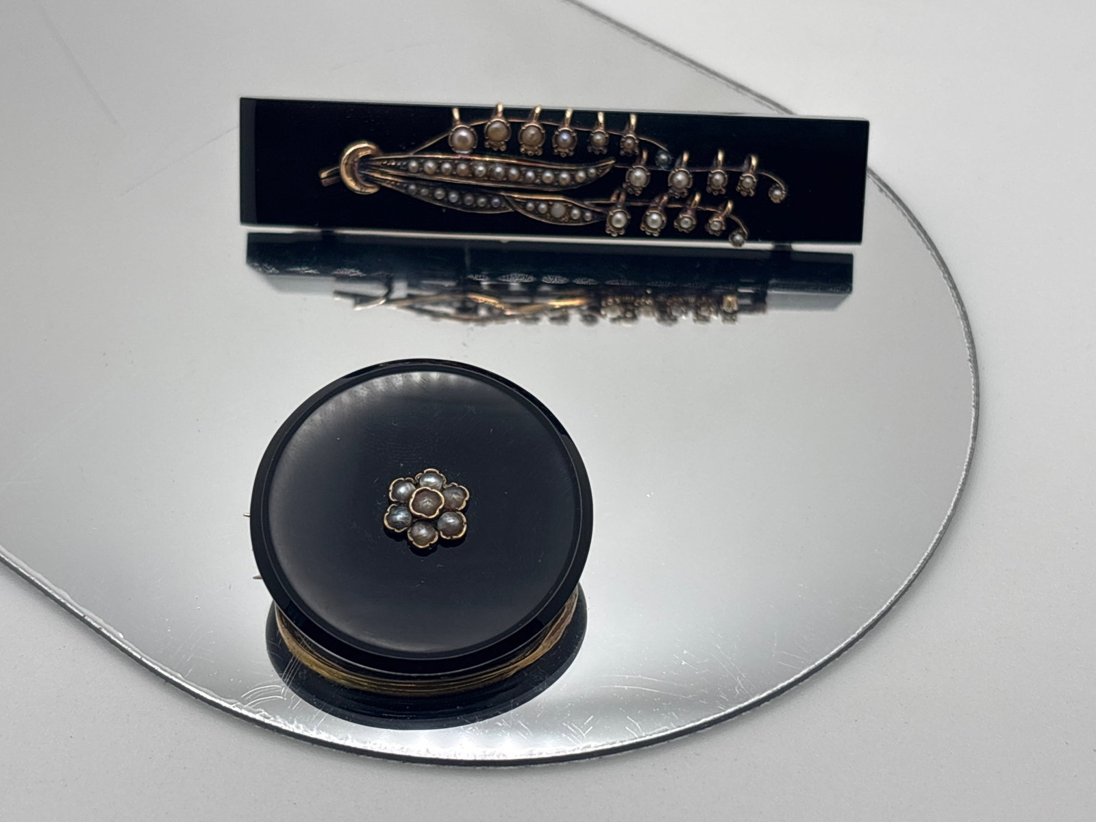 Two Victorian Onyx and Seed Pearl Brooches: To include a Victorian bar brooch mounted in a seed pearl and gold-filled lily of the valley decoration, 2-5/8in long x 1/2in wide; and a seed pearl and 14K (tested) button pin/pendant, 1-1/4in