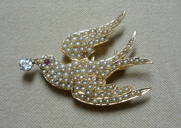 Lady's Watch Pin: Lady's watch pin formed like a flying bird, possibly dove, set in 14K yellow gold (marked). Body is encrusted with seed pearls; beak contains an Old European cut diamond (apx. 0.15ct); ruby eye. 36mm 